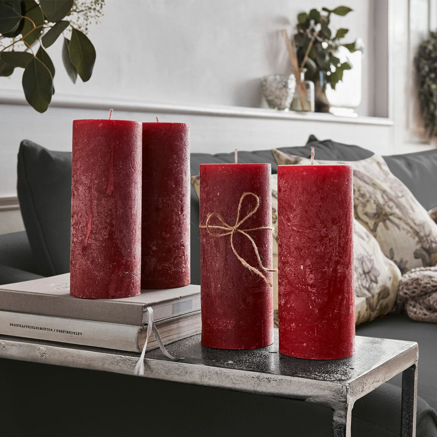 Kerze 4er Set Homel Vier rote Wachskerzen als Dekoration auf einem Metalltisch im Wohnzimmer mit Kissen