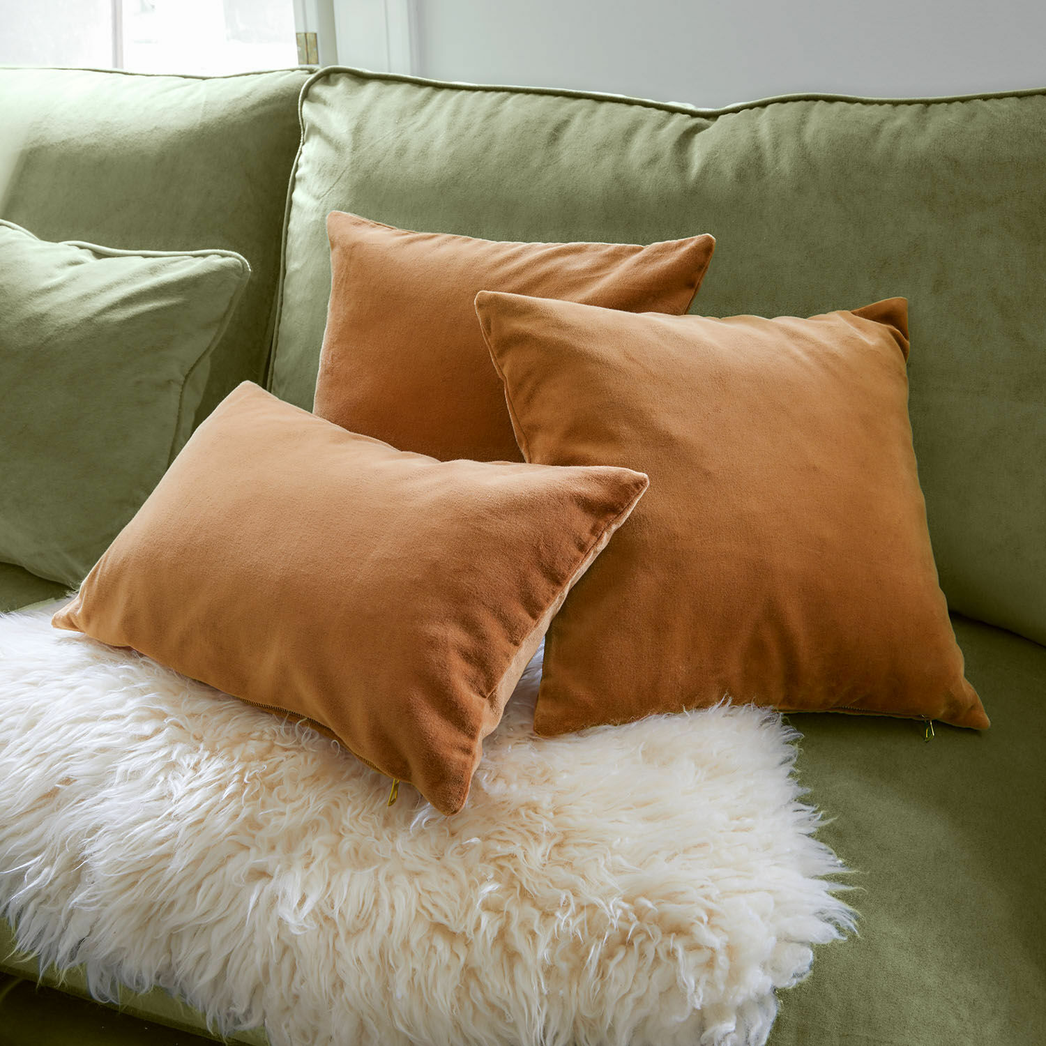 Kissenhülle 3er Set Shahrine Drei braune Kissen aus weichem Stoff auf grünem Sofa mit weissem Fellplaid für gemütliche Einrichtung