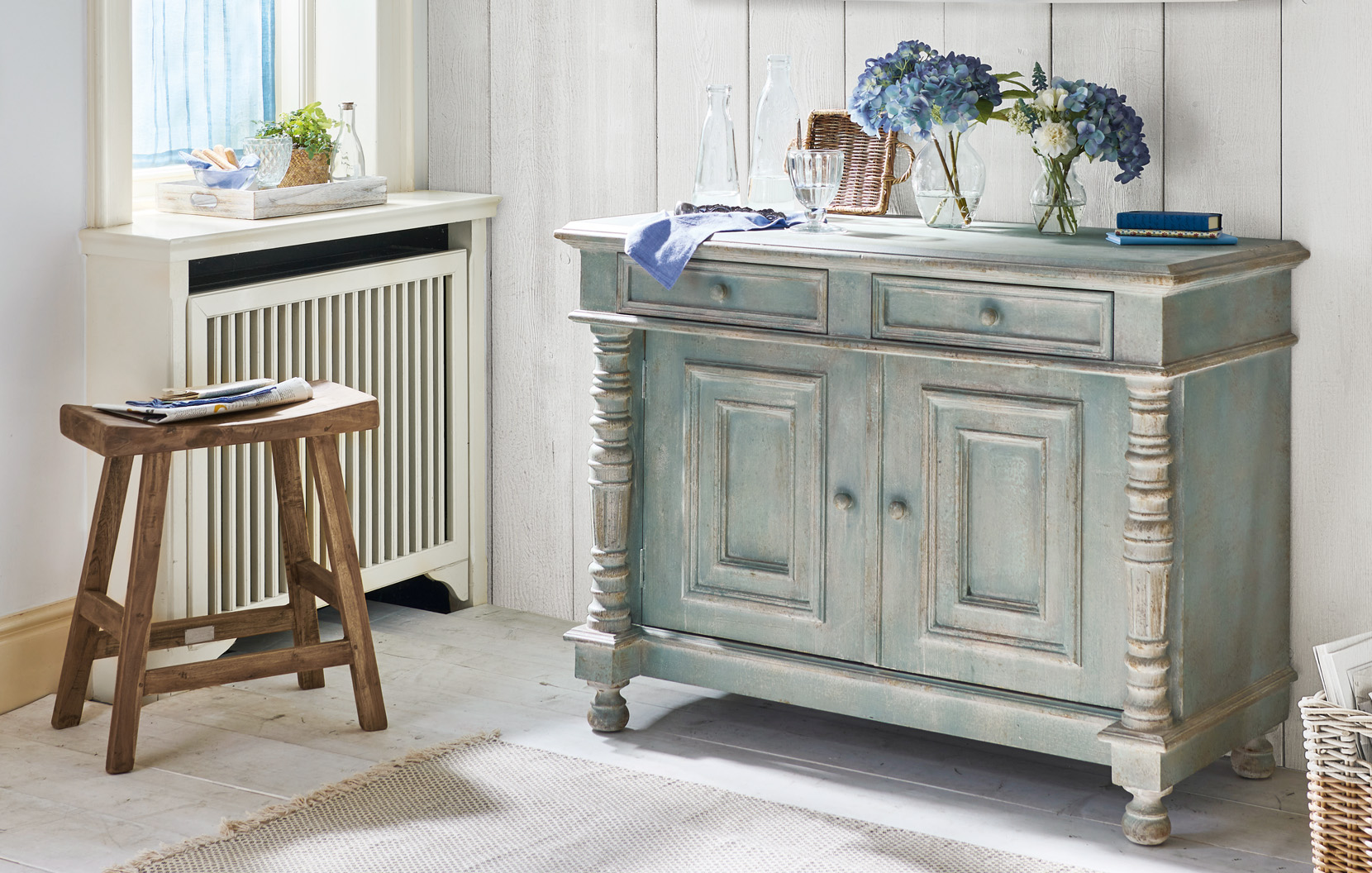 Shabby-Chic-Kommode aus Holz in Grün-Grau mit dekorativen Blumen und Glasflaschen