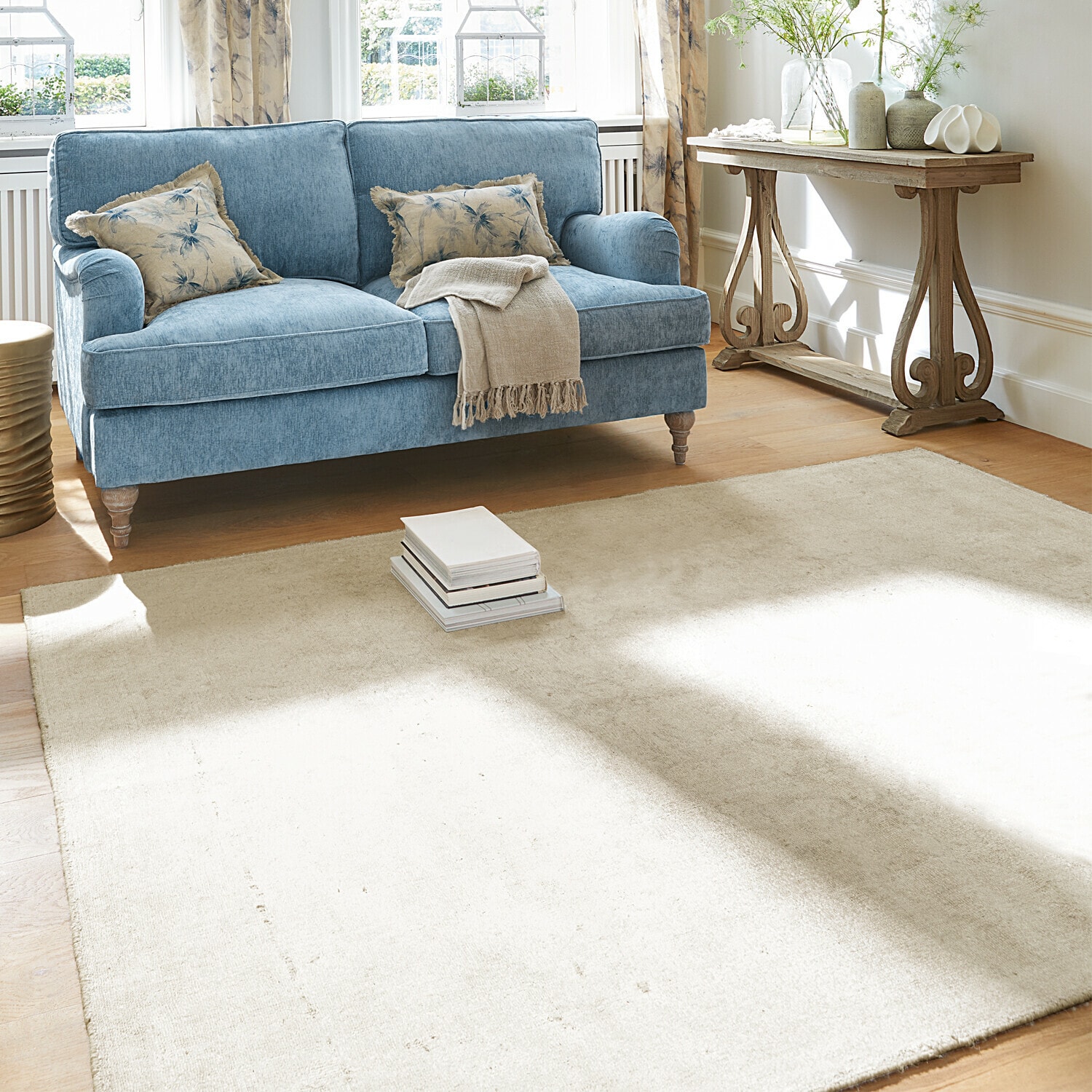 Hellblaues Stoffsofa mit beiger Decke und floralen Kissen in hellem Wohnzimmer