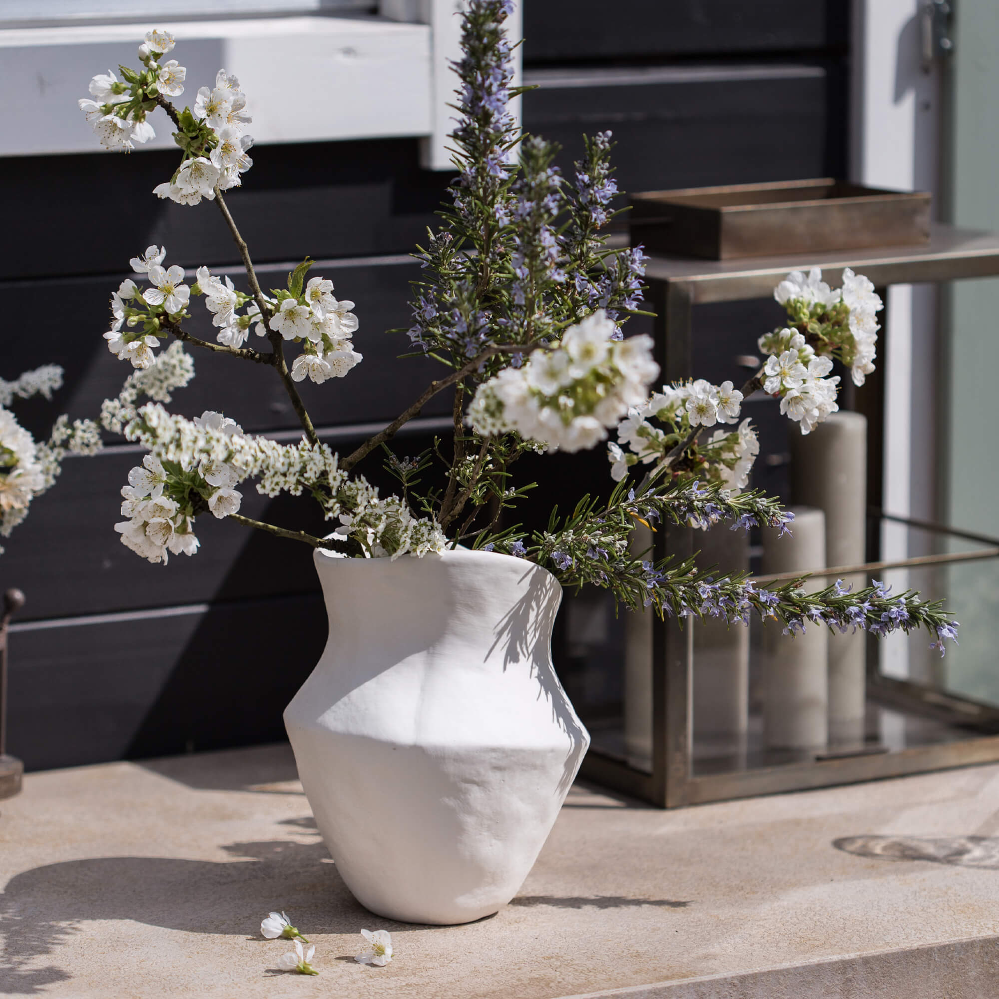 Weisse Keramikvase mit Blumen und Zweigen auf dekorativem Aussentisch
