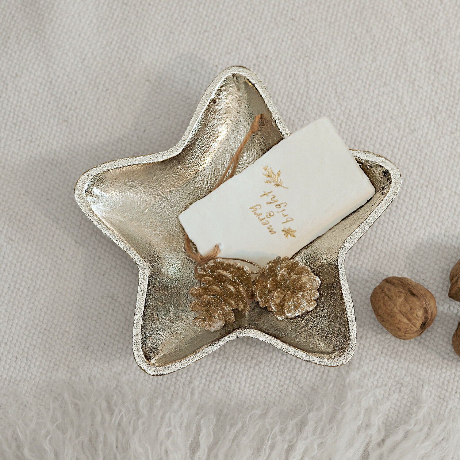 Dekorative Sternschale aus silbernem Metall mit goldenen Zapfen und Wallnüssen auf hellem Stoff