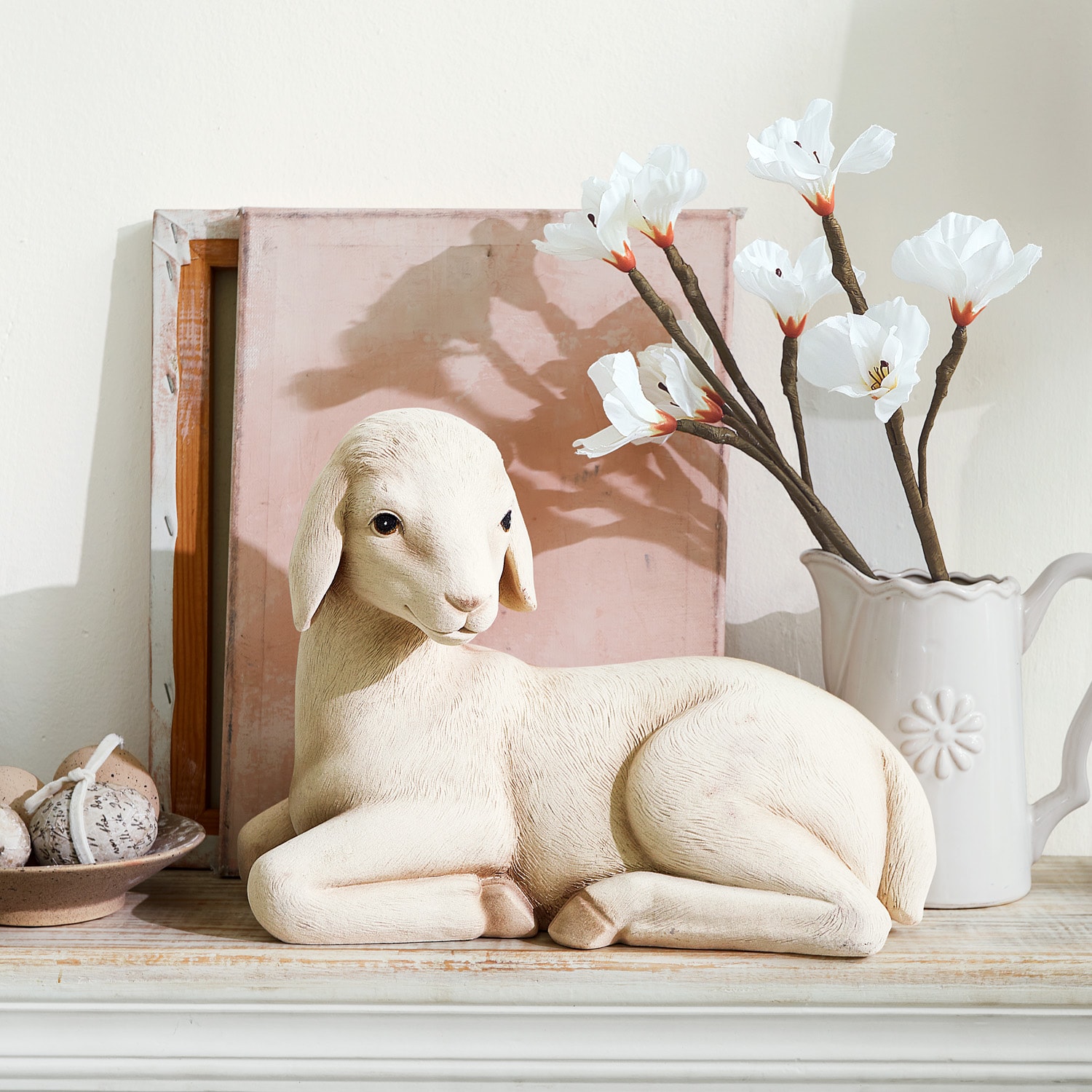 Dekorative Schaf-Figur in hellem Farbton auf Holzregal mit weißen Blumen und Deko