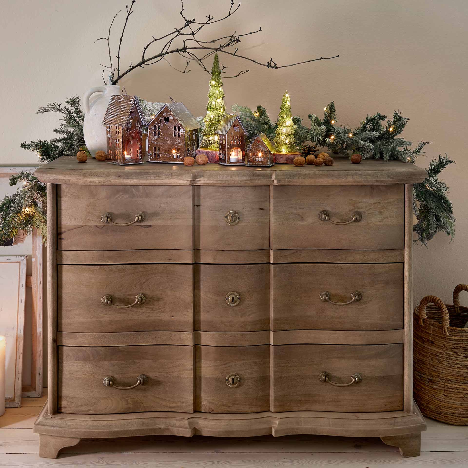 Weihnachtsdekoration mit Metalllaternen in Hausform und grünen beleuchteten Tannen auf Holzkommode