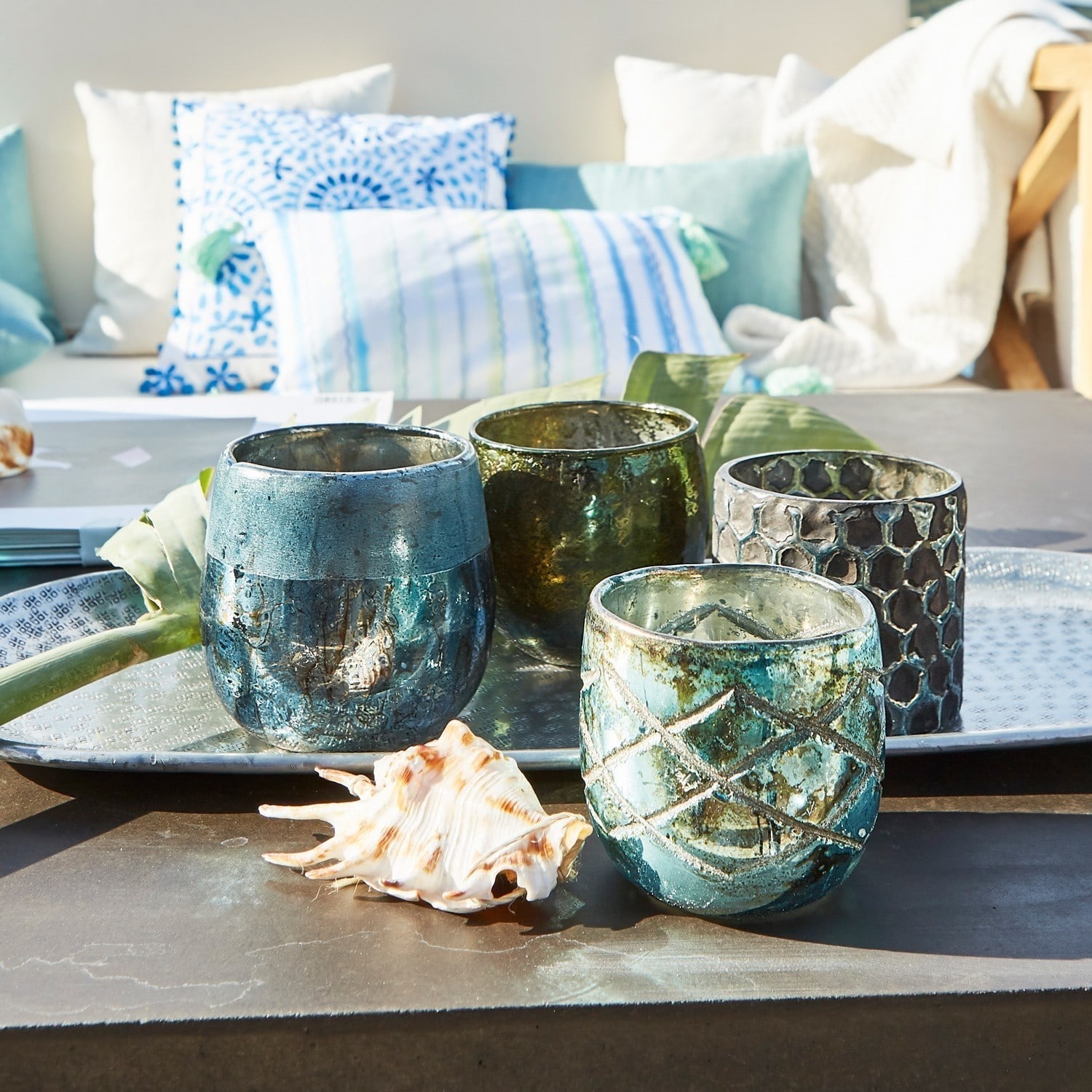 Set mit vier blauen und grünen Glas-Teelichthaltern auf Metalltablett mit Muschel-Dekor