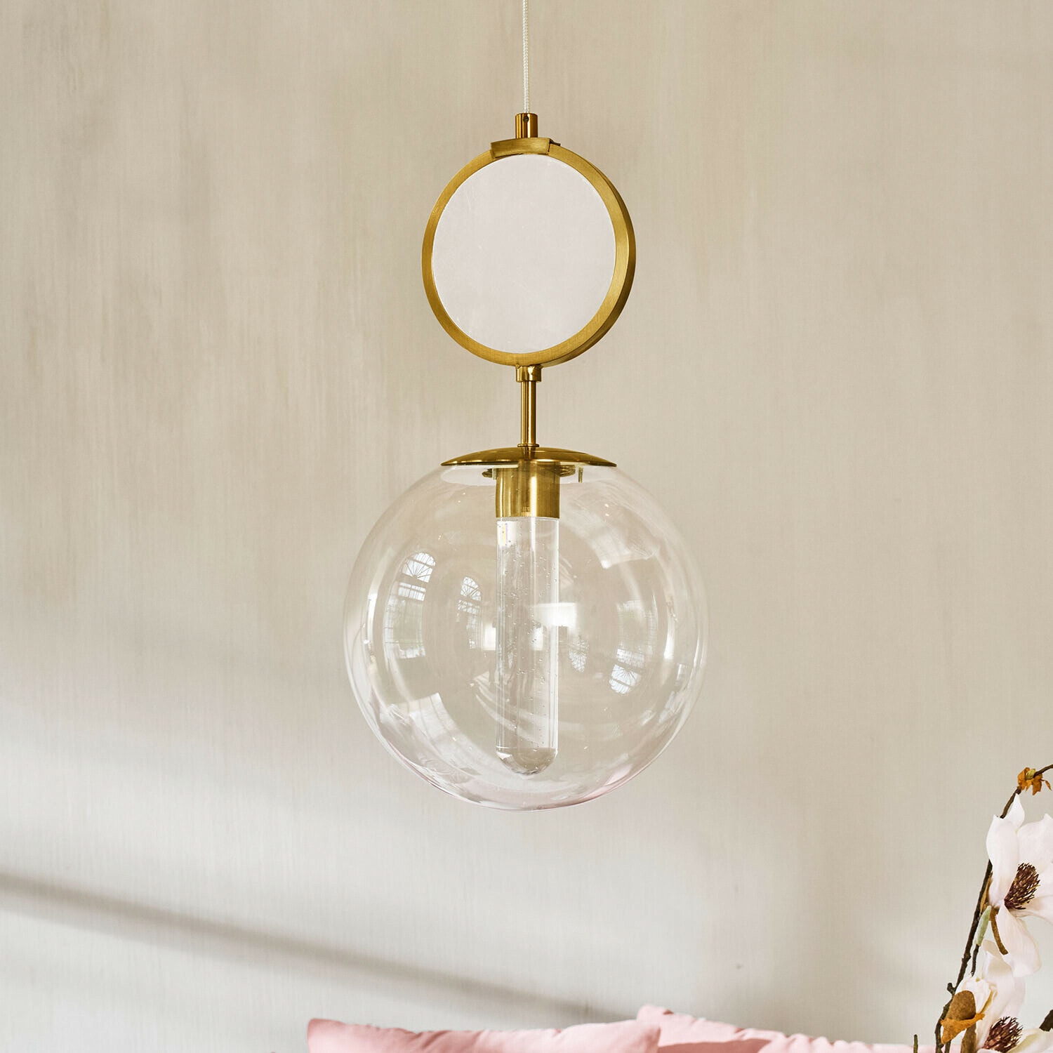 LED-Hängelampe Corvane Goldene Hängeleuchte mit klarem Glaskugel und rundem dekorativem Element vor hellem Wandhintergrund