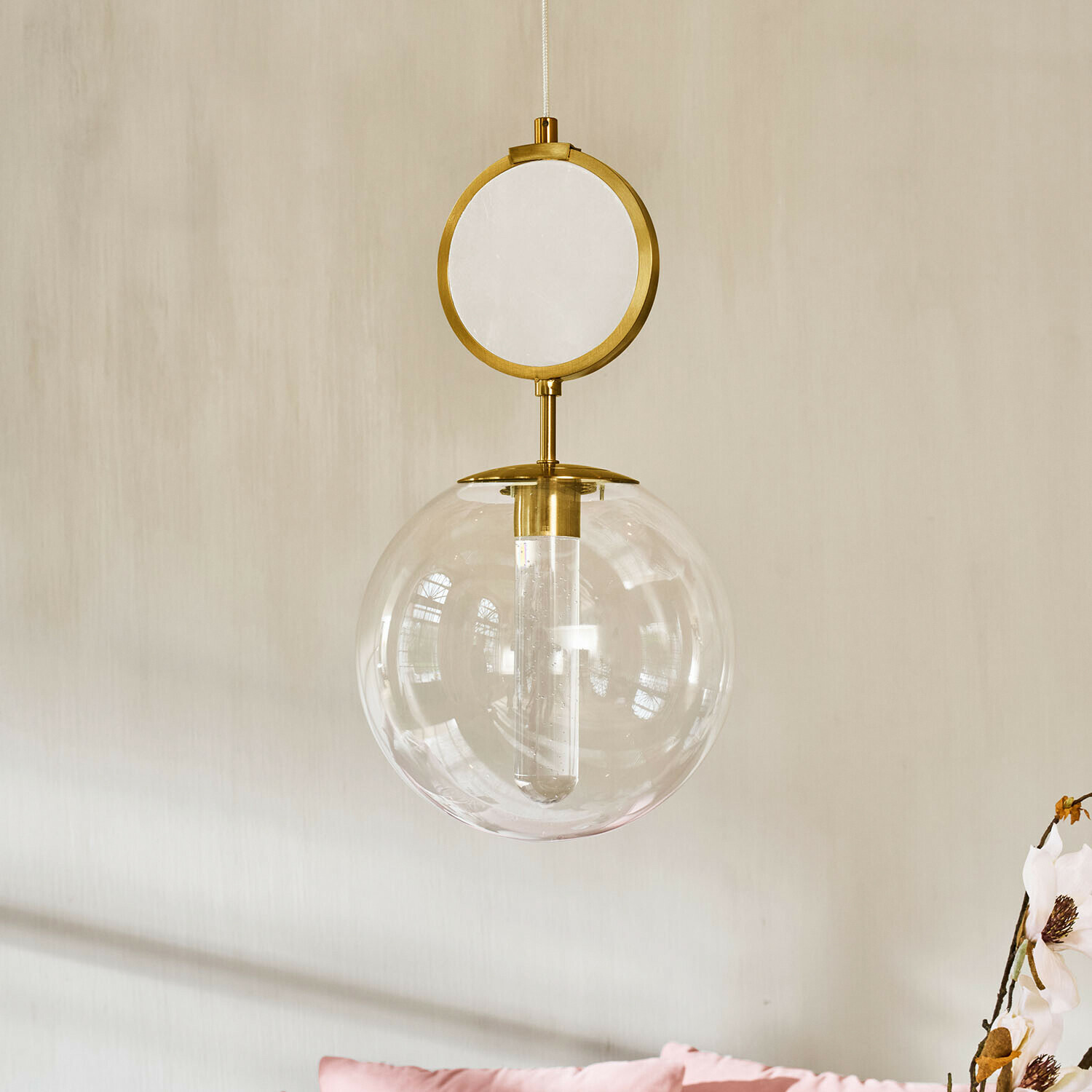 LED-Hängelampe Corvane Goldene Hängeleuchte mit klarem Glaskugel und rundem dekorativem Element vor hellem Wandhintergrund