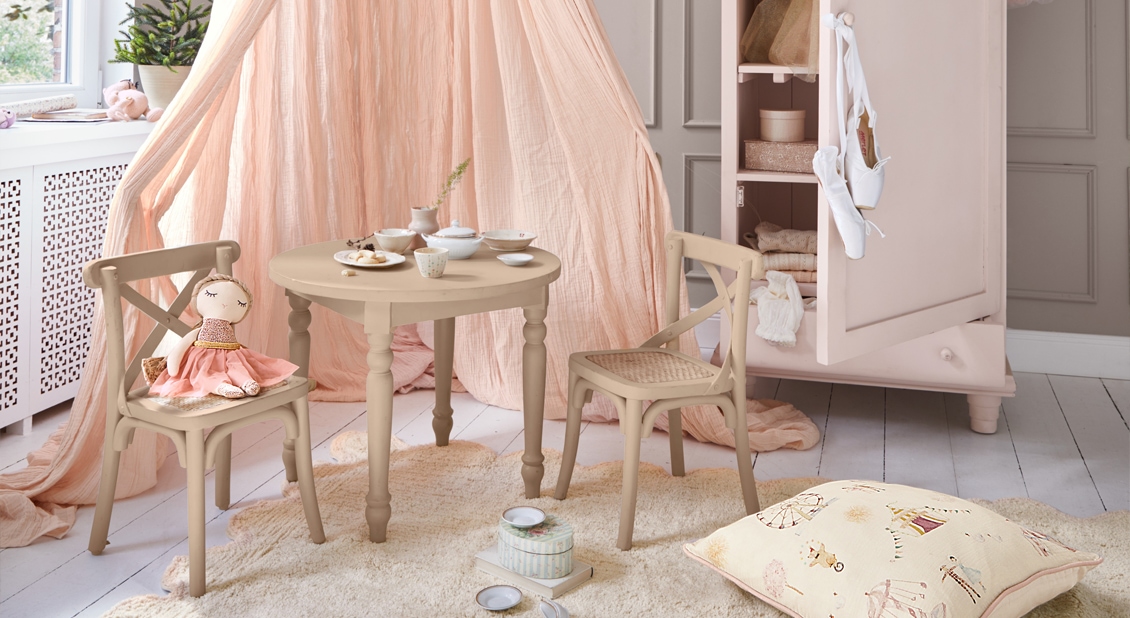 Beiger Holztisch und Kinderstühle mit Puppe und puderrosa Vorhang in pastellfarbenem Kinderzimmer