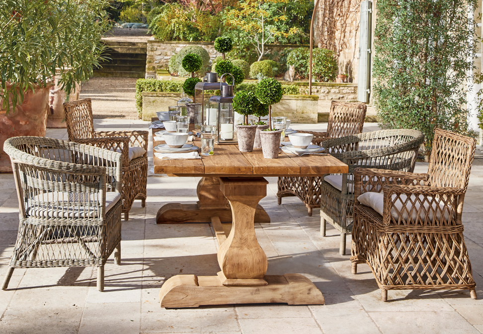 Holz-Gartentisch mit Korbsesseln und Pflanzendekoration auf mediterraner Terrasse