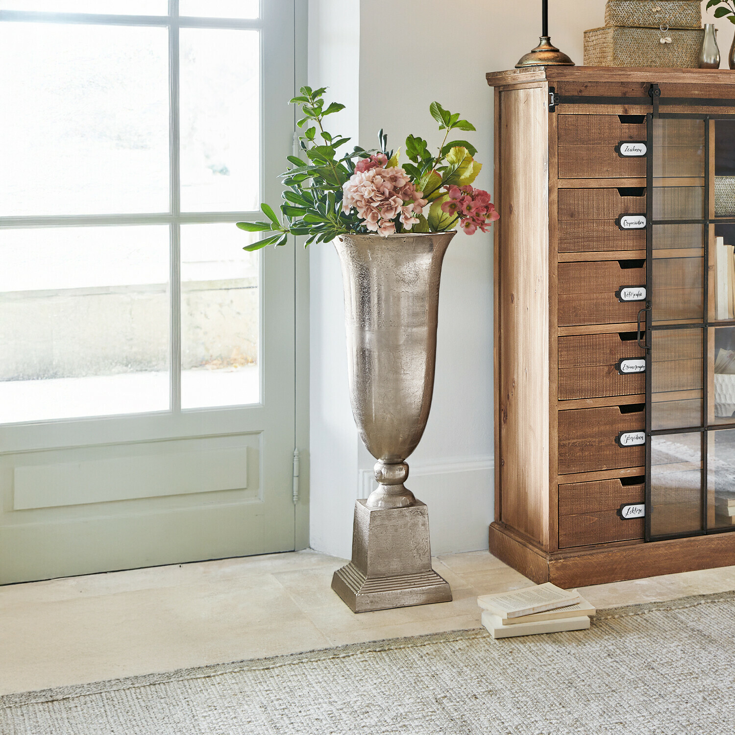 Bodenvase Belfort Hohe silberne Metallvase mit Blumen neben einem Holzschrank in einem hellen Raum