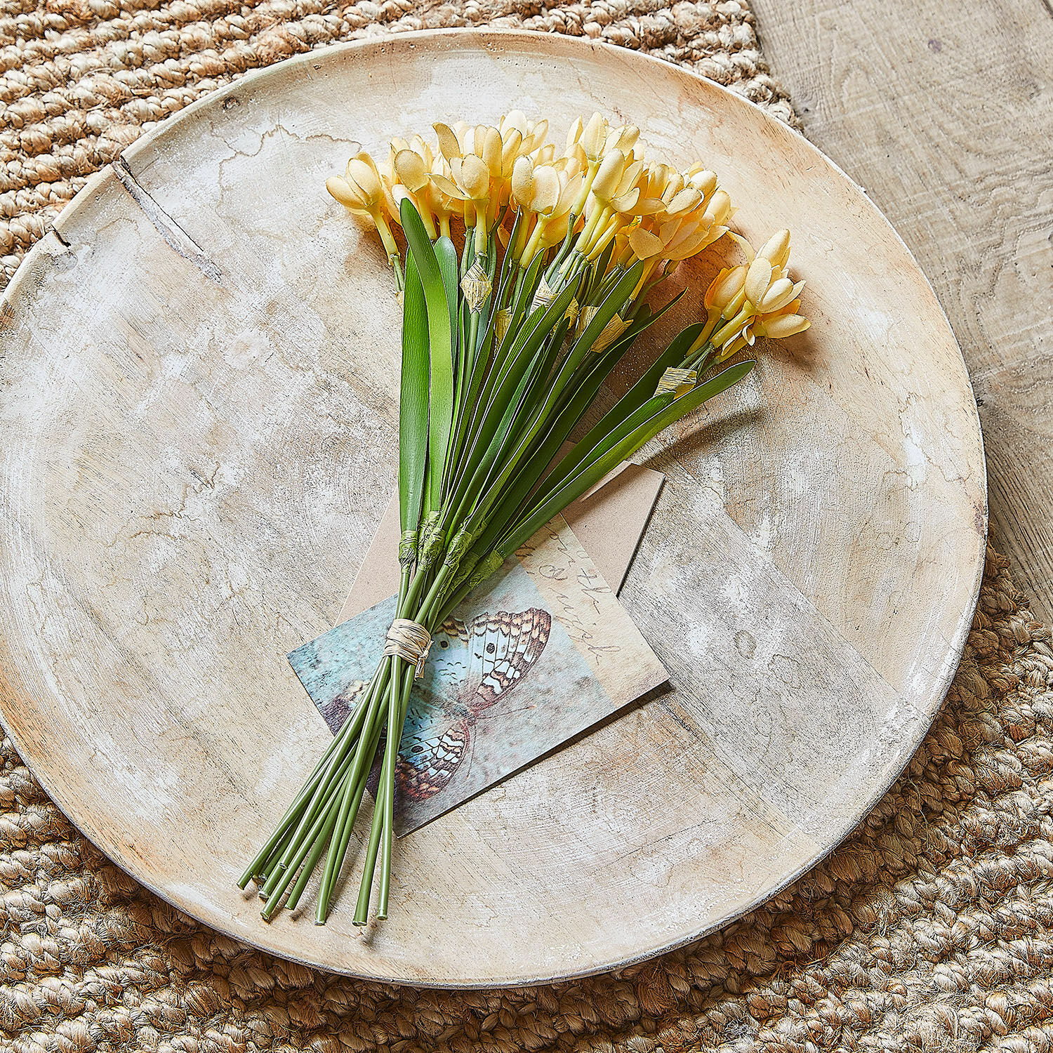 Strauuss gelber künstlicher Blumen auf einem Holztablett auf Juteteppich, Wohnaccessoire
