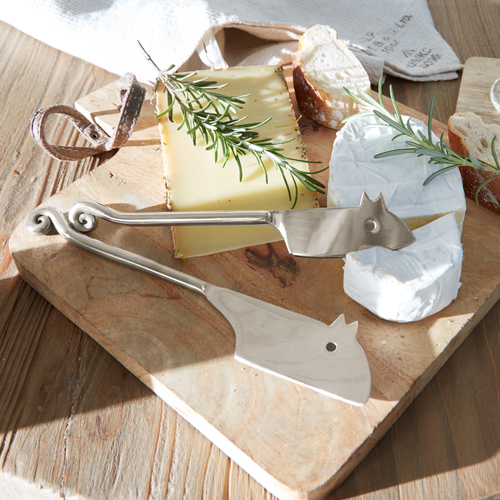 Set aus Edelstahls-Käsemessern auf Holzbrett mit Käse und Kräutern, Küchenutensilien