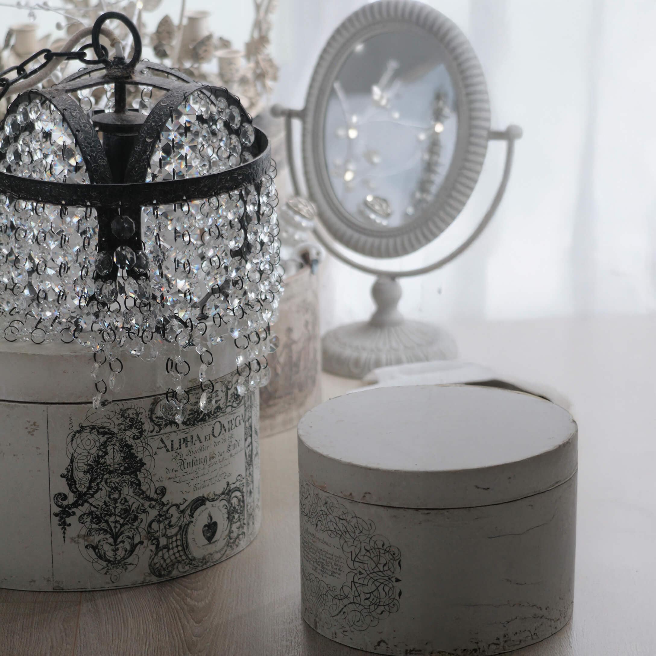 Kristall-Kronleuchter mit schwarzem Metallrahmen auf weisser Vintage-Box mit Ornamenten