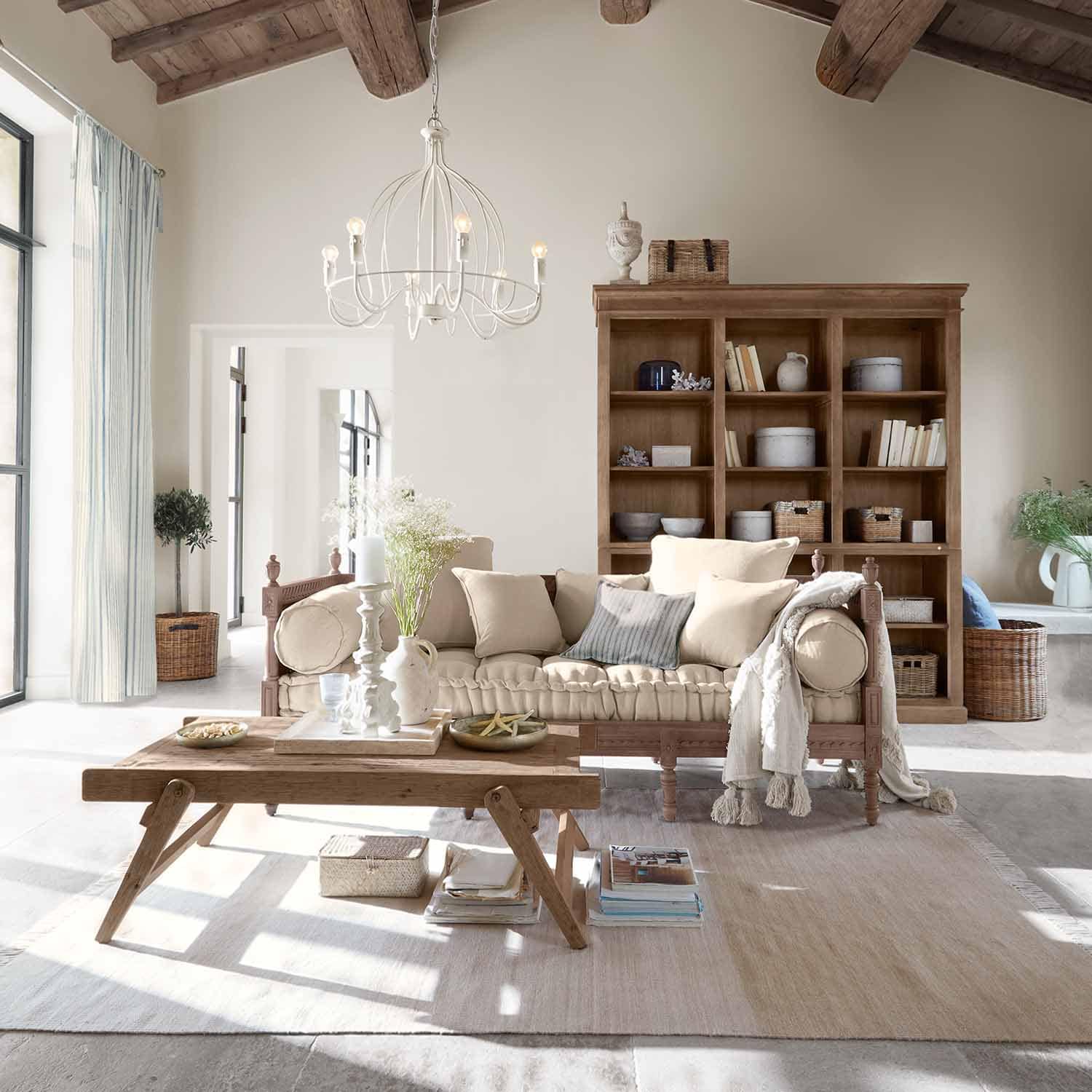 Gemütliches Wohnzimmer mit Holzsofa und beigen Kissen sowie rustikalem Holzcouchtisch und Regal im Hintergrund