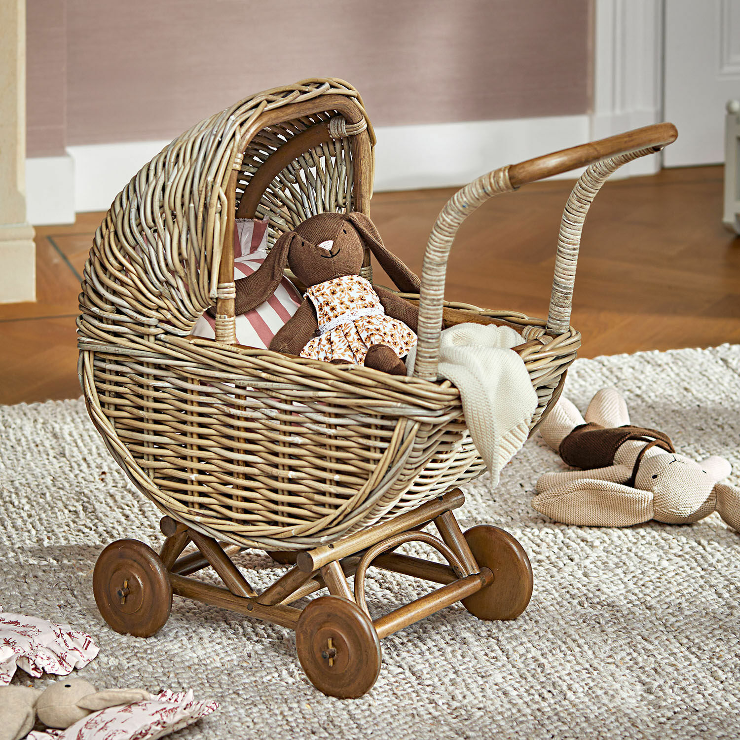 Puppenwagen Fableton Wickelwagen aus Korbgeflecht mit Holzrädern und Kuscheltieren auf Teppich im Kinderzimmer