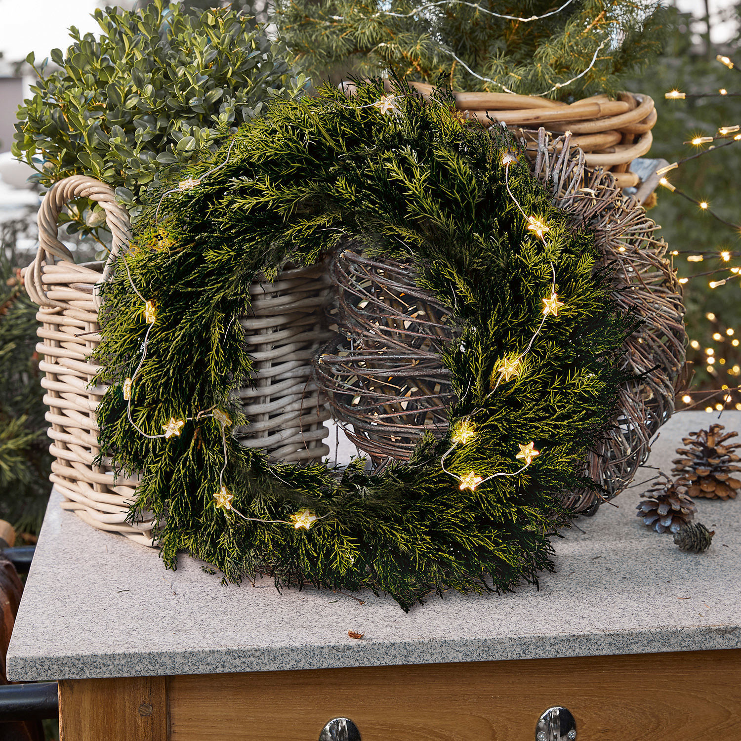 Kranz Évres Grüner Weihnachtskranz aus Zweigen mit Stern-Lichterkette auf Steinplatte neben Korb aus Weidenholz