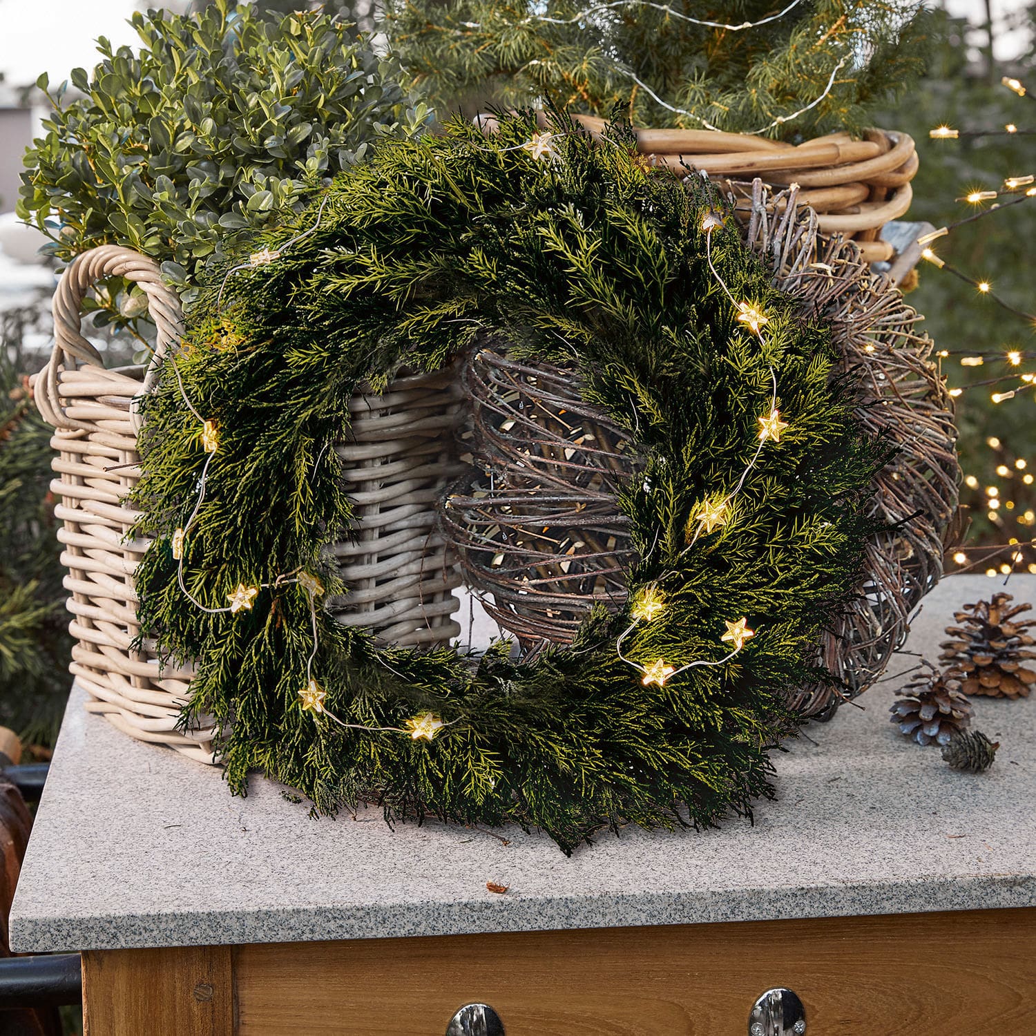 Kranz Évres Grüner Weihnachtskranz aus Zweigen mit Stern-Lichterkette auf Steinplatte neben Korb aus Weidenholz