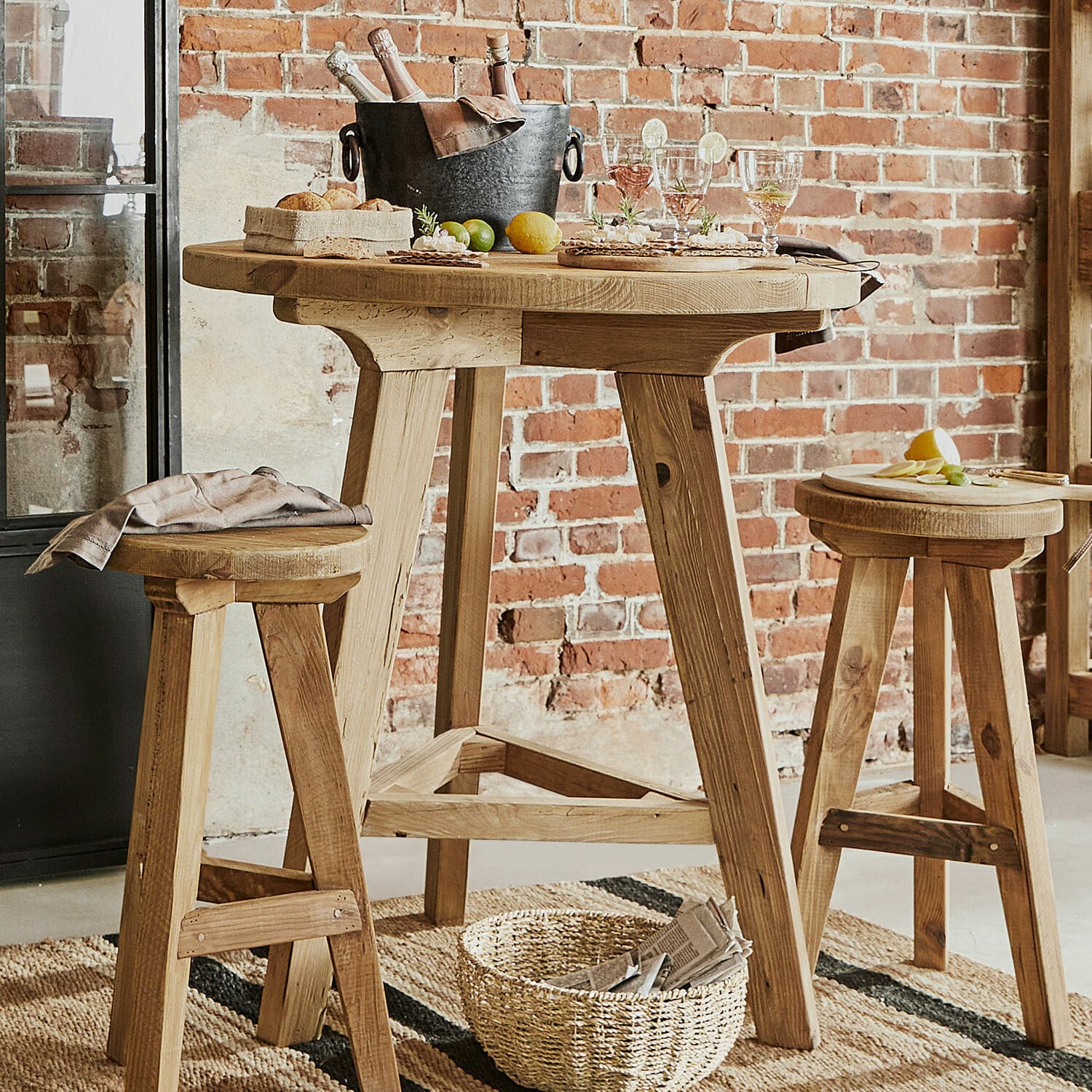 Stehtisch Stonington Hoher Holztisch mit zwei Hockern aus Naturholz vor roter Ziegelwand im Loft-Stil