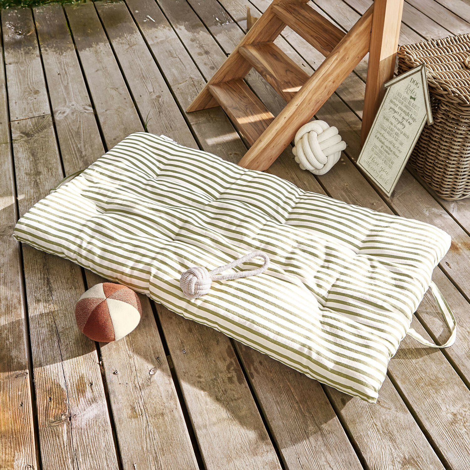 Gepolstertes grün gestreiftes Bodenkissen auf Holzterrasse mit Hundespielzeug