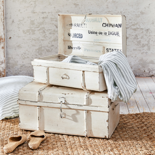 Weisse Vintage-Holzkisten mit Gebrauchsspuren, Textilien und Hausschuhen auf Juteteppich