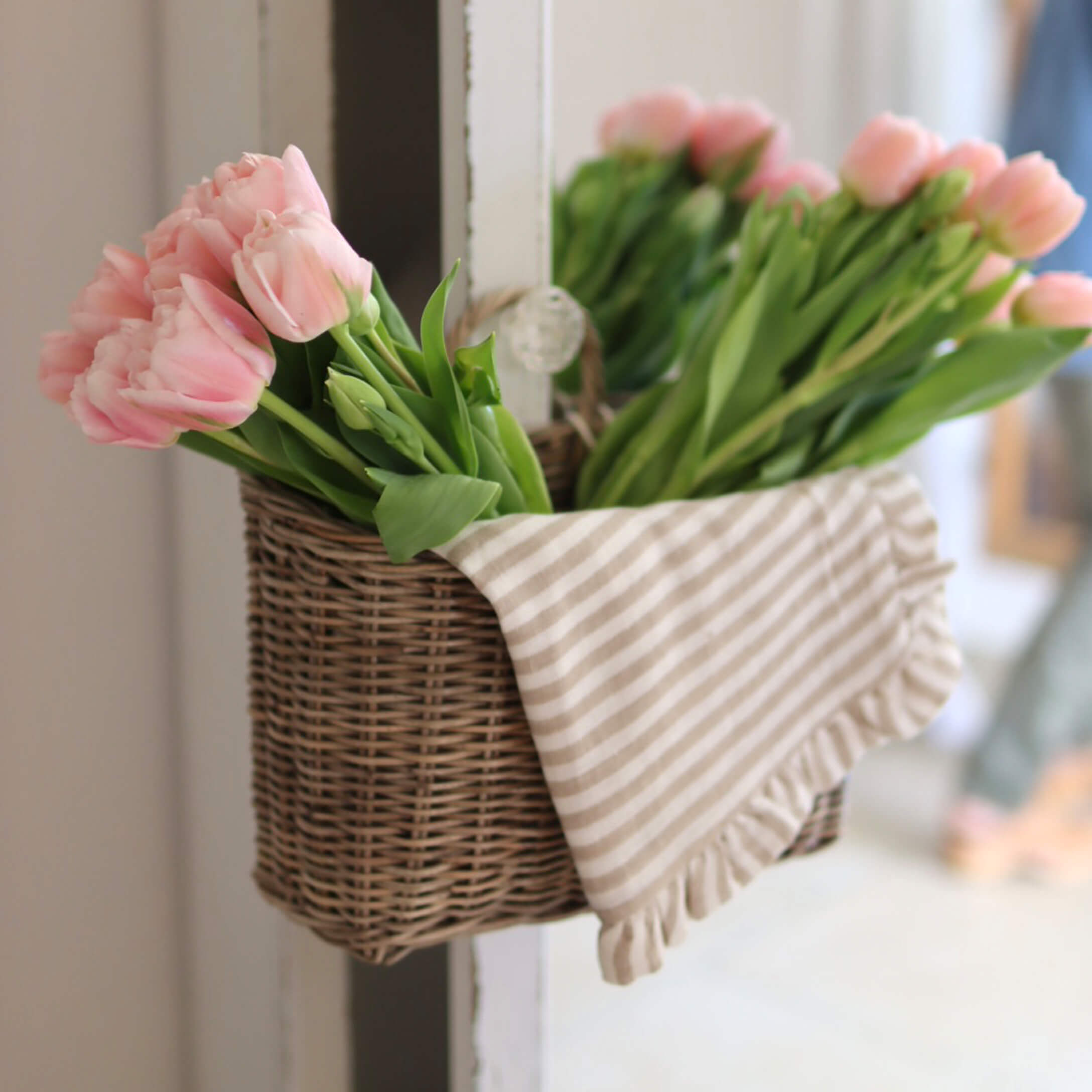 Weidenkorb mit rosa Tulpen und gestreiftem Baumwolltuch als Wohnaccessoire