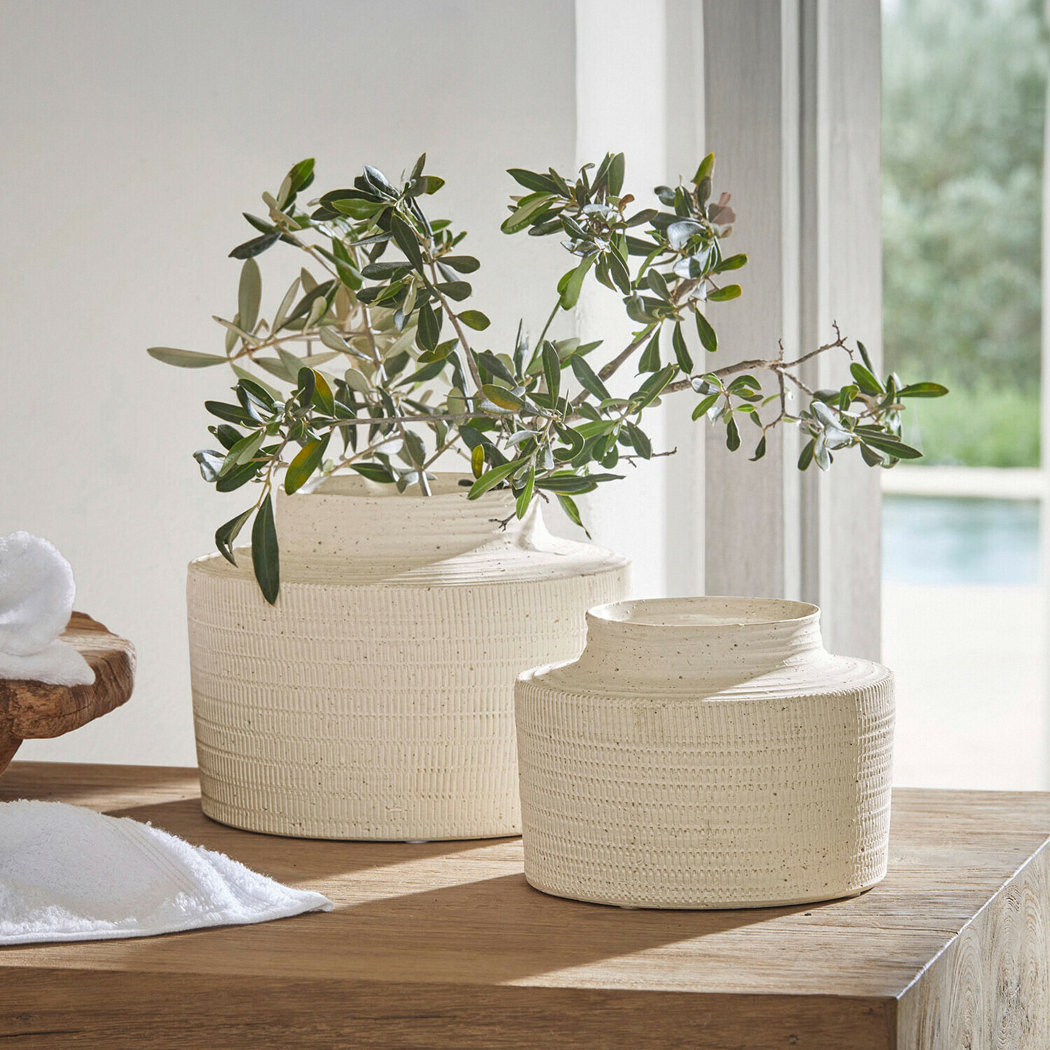 Zwei cremefarbene Keramikvasen mit Struktur auf Holztisch mit grünen Zweigen