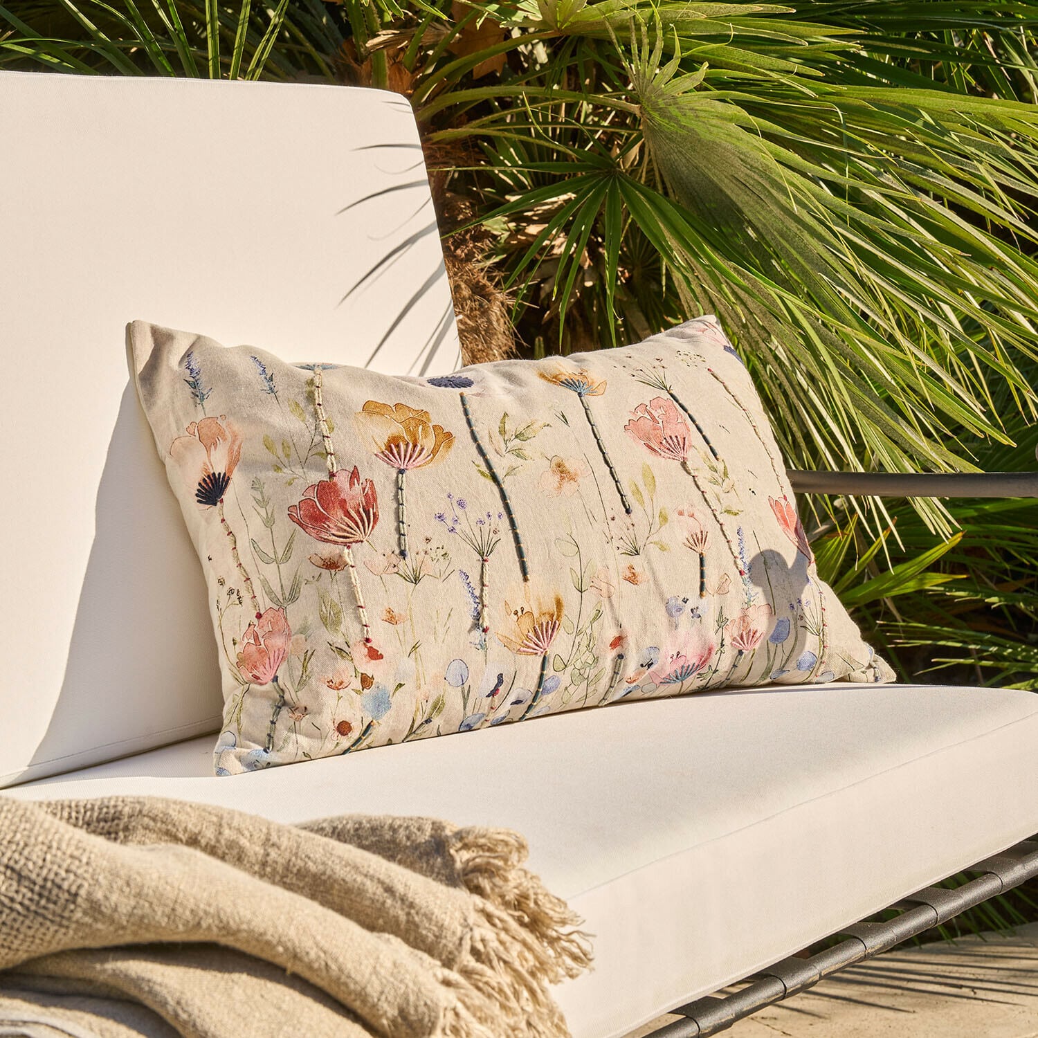 Beiges Dekokissen mit Blumenmuster auf hellem Gartensessel mit Decke