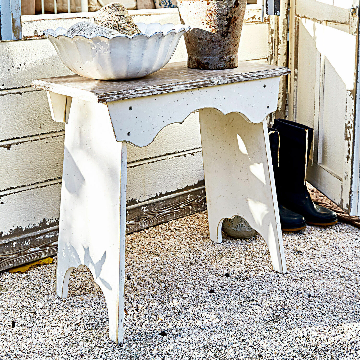 Hocker Fria Weisser Holztisch mit Shabby-Chic-Oberfläche auf Kiesboden, dekorative Schale und schwarze Stiefel