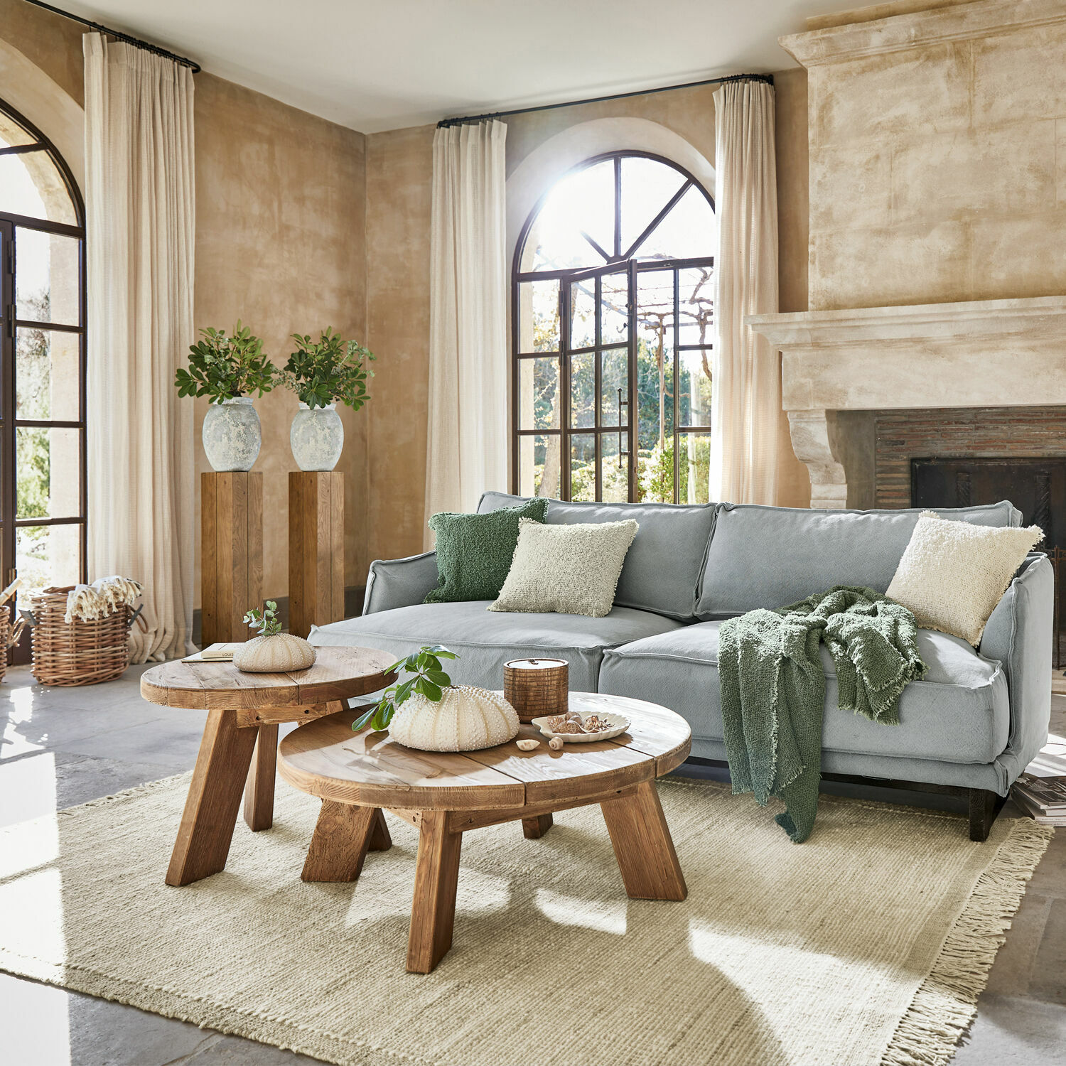 Gemütliches Wohnzimmer mit grauem Sofa, rustikalen Holztischen und hellem Naturteppich