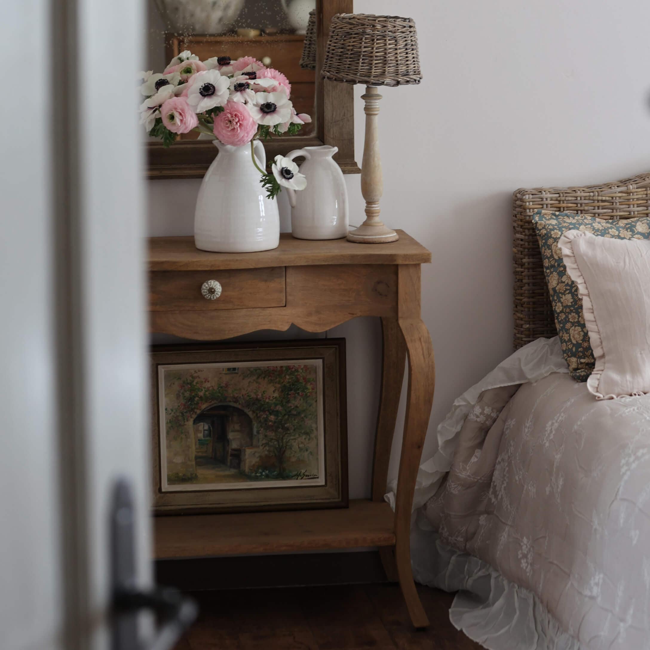 Holztisch mit weissen Keramikvasen und Blumen neben Bett mit geflochtenem Kopfteil