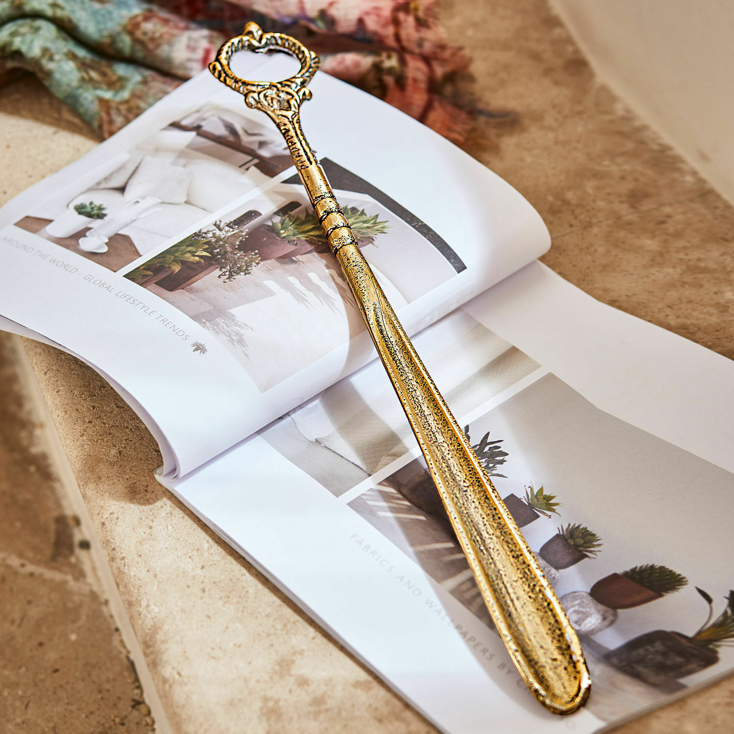 Schuhlöffel Lucas Goldfarbener Metallschuhlöffel mit verziertem Griff, liegend auf offenem Wohnmagazin
