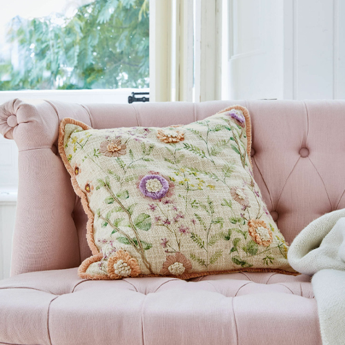 Dekoratives Kissen mit pastellfarbener Blumenstickerei auf rosa Sofa, weiches Material
