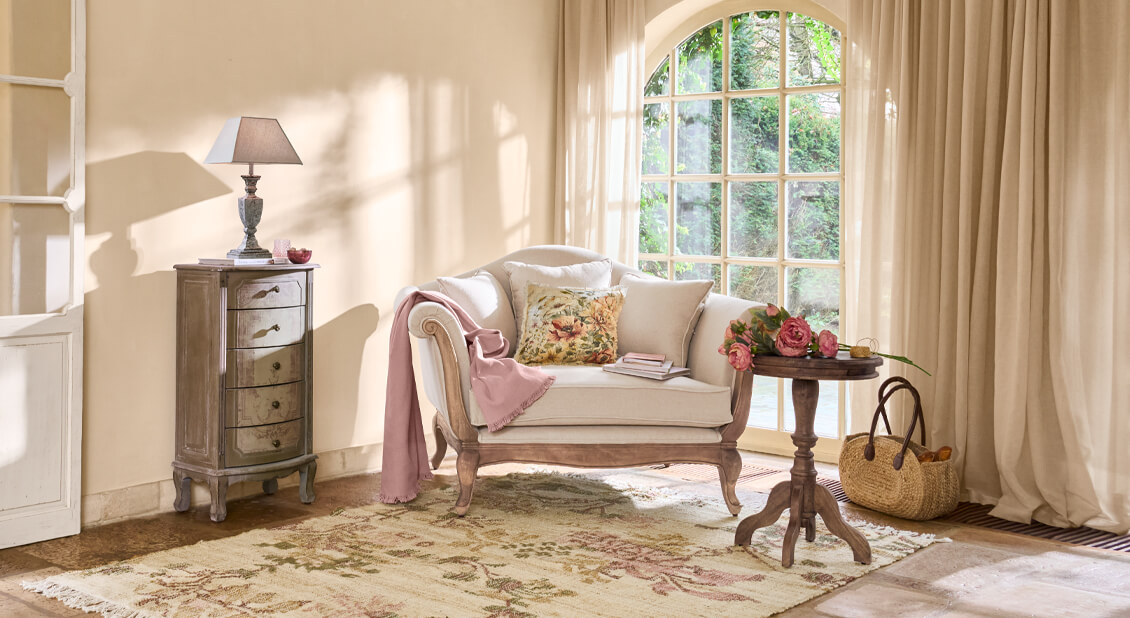 Gemütliches Wohnzimmer mit beigem Sofa, rosa Decke und Holztisch mit Blumen, natürliches Licht