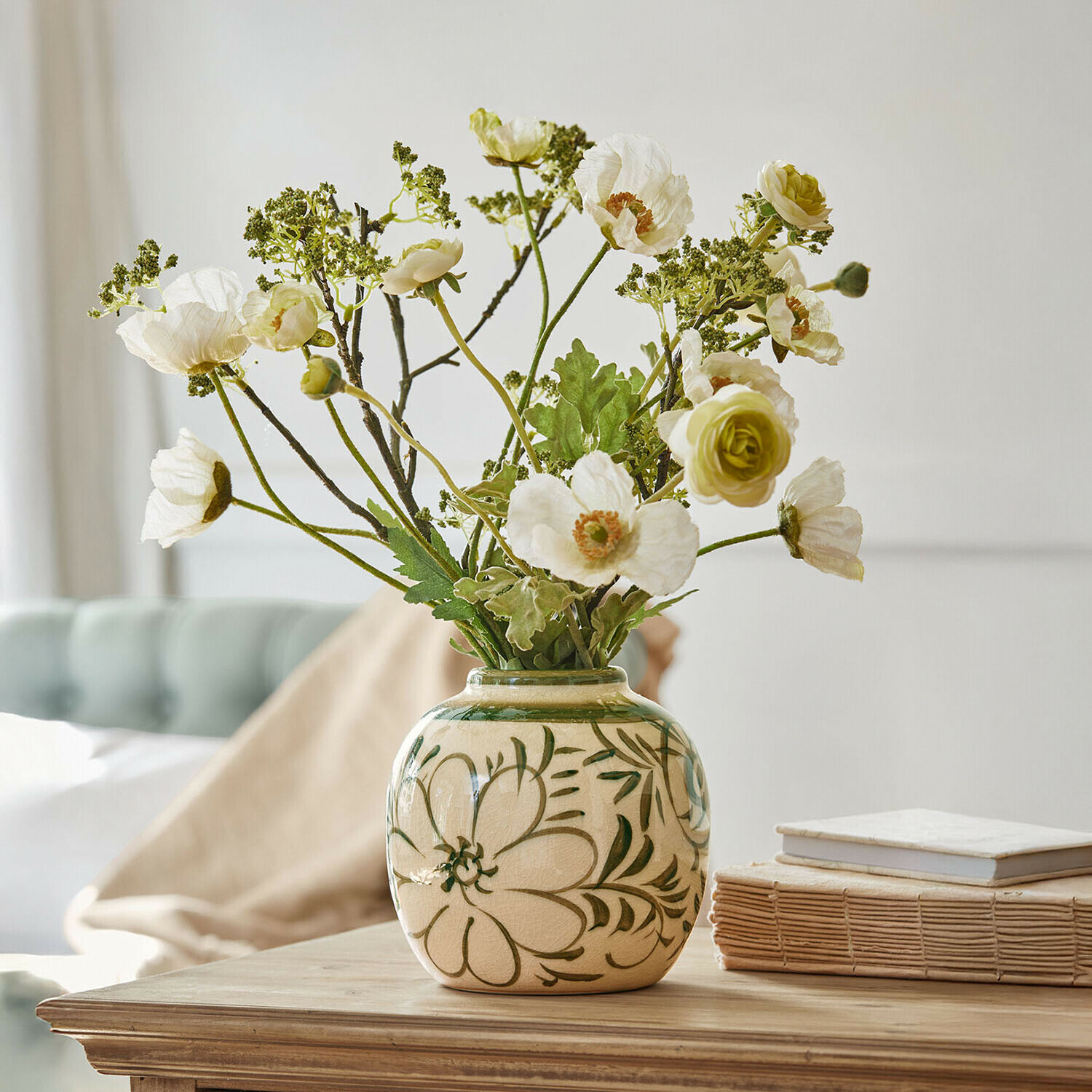 Keramikvase mit grünen Blumenmustern und weißen künstlichen Blumen auf Holztisch dekorativ