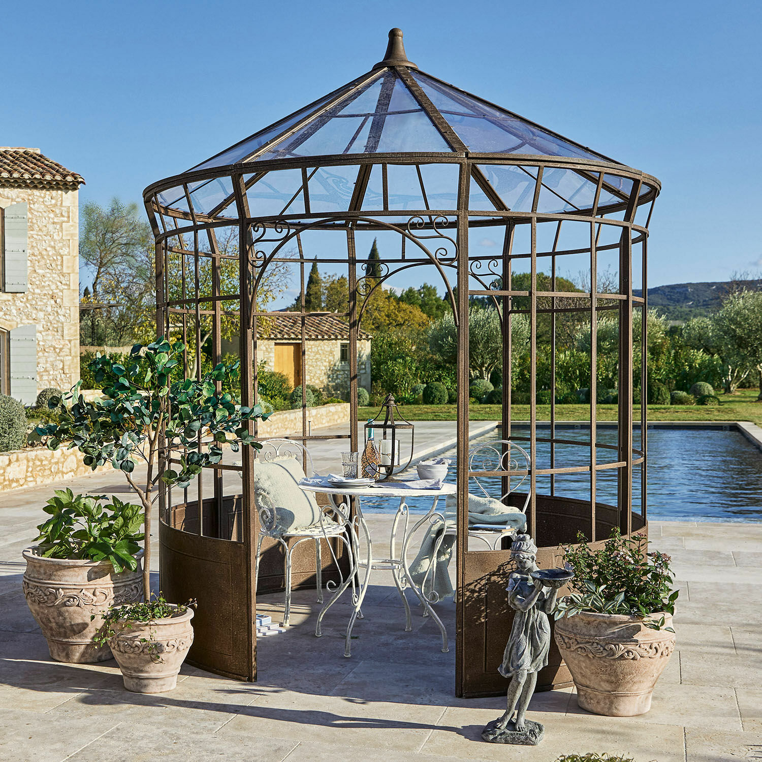 Pavillon Murillo Dekorativer Gartenpavillon aus rostfarbenem Metall mit weissem Tisch und Stühlen auf Terrasse beim Pool