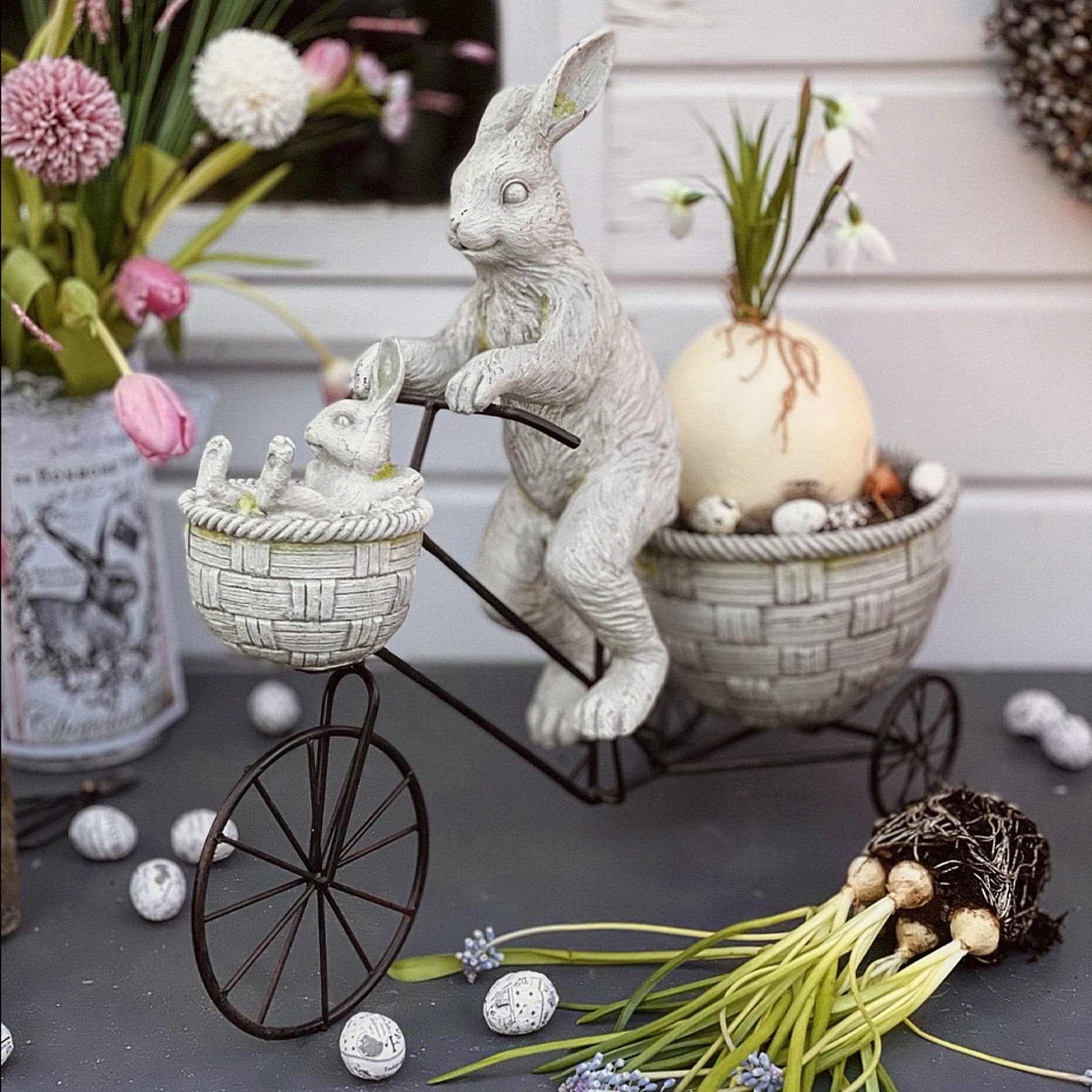 Osterdekoration mit weissen Hasen aus Kunststoff auf Metallvelo mit Körben und Blumen