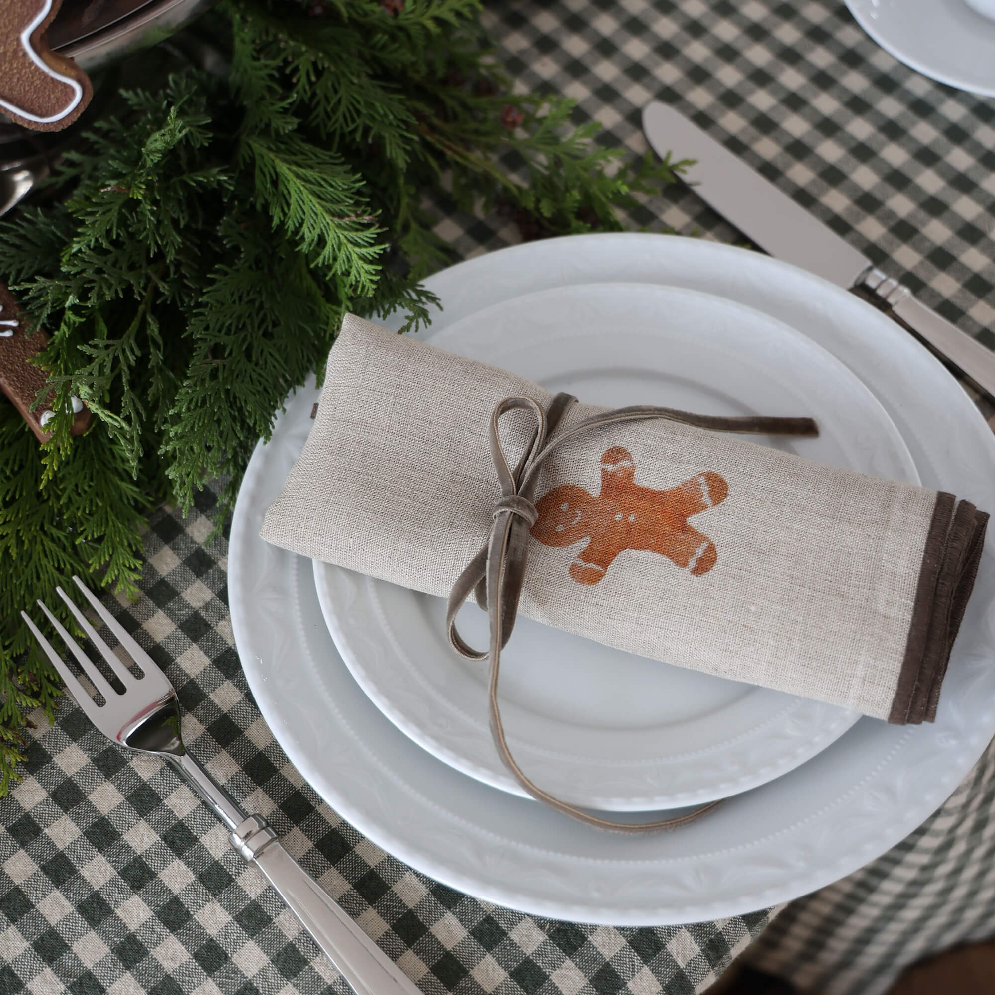 Beige Leinenserviette mit Lebkuchenmännchen-Motiv und grauem Band auf weissem Teller
