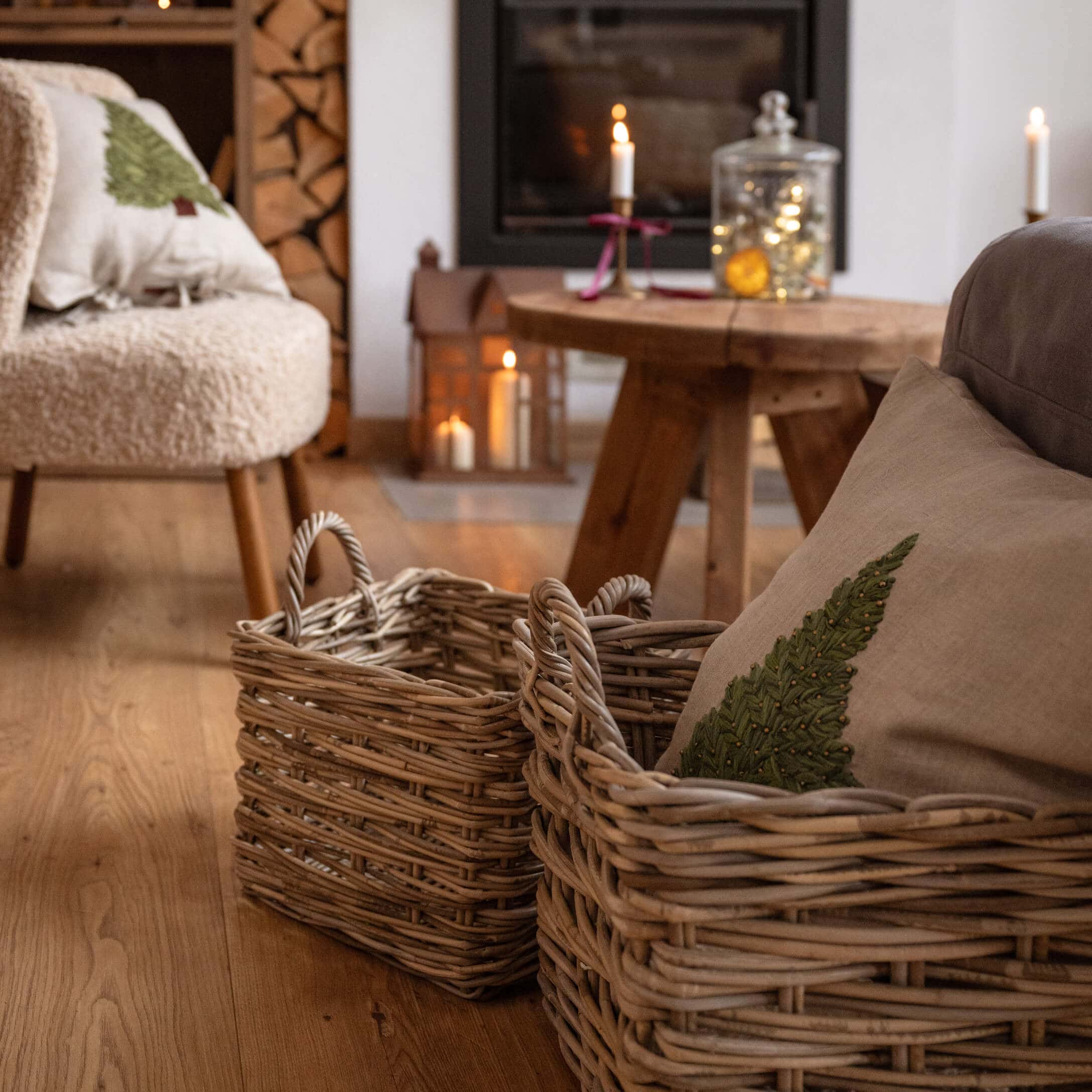 Zwei naturfarbene Weidenkörbe auf Holzboden in gemütlichem Wohnzimmer mit Kamin