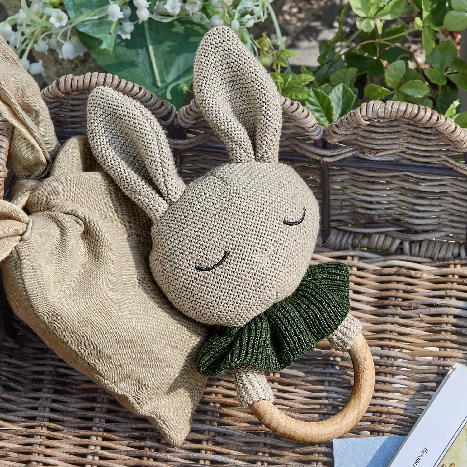 Spielzeugring Cuddlecloud Beige gestrickte Hasenrassel mit grünem Kragen und Holzring auf Korbhintergrund