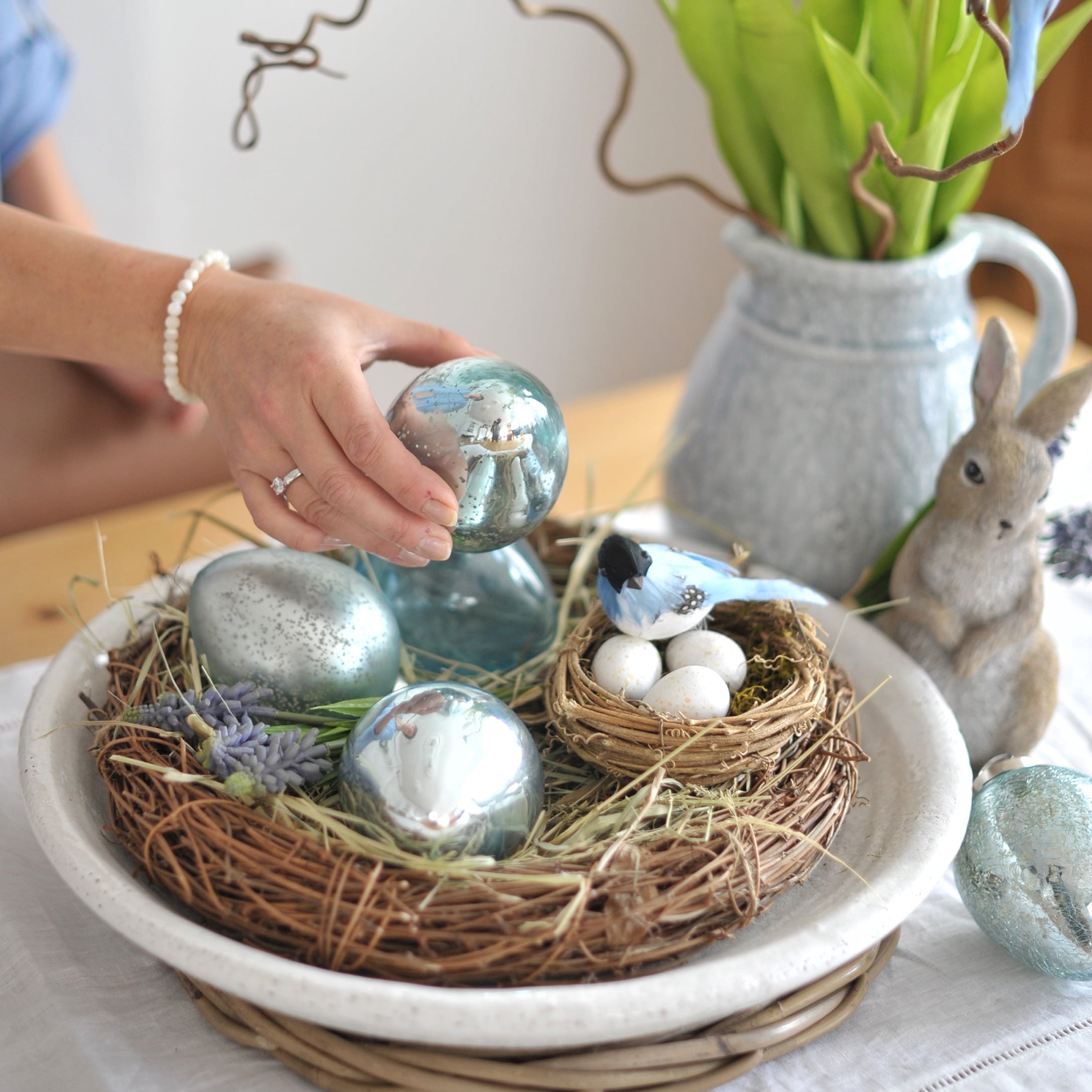 Osterdekoration mit blauen Glaseiern und Nest mit weissen Eiern auf einem Holztisch