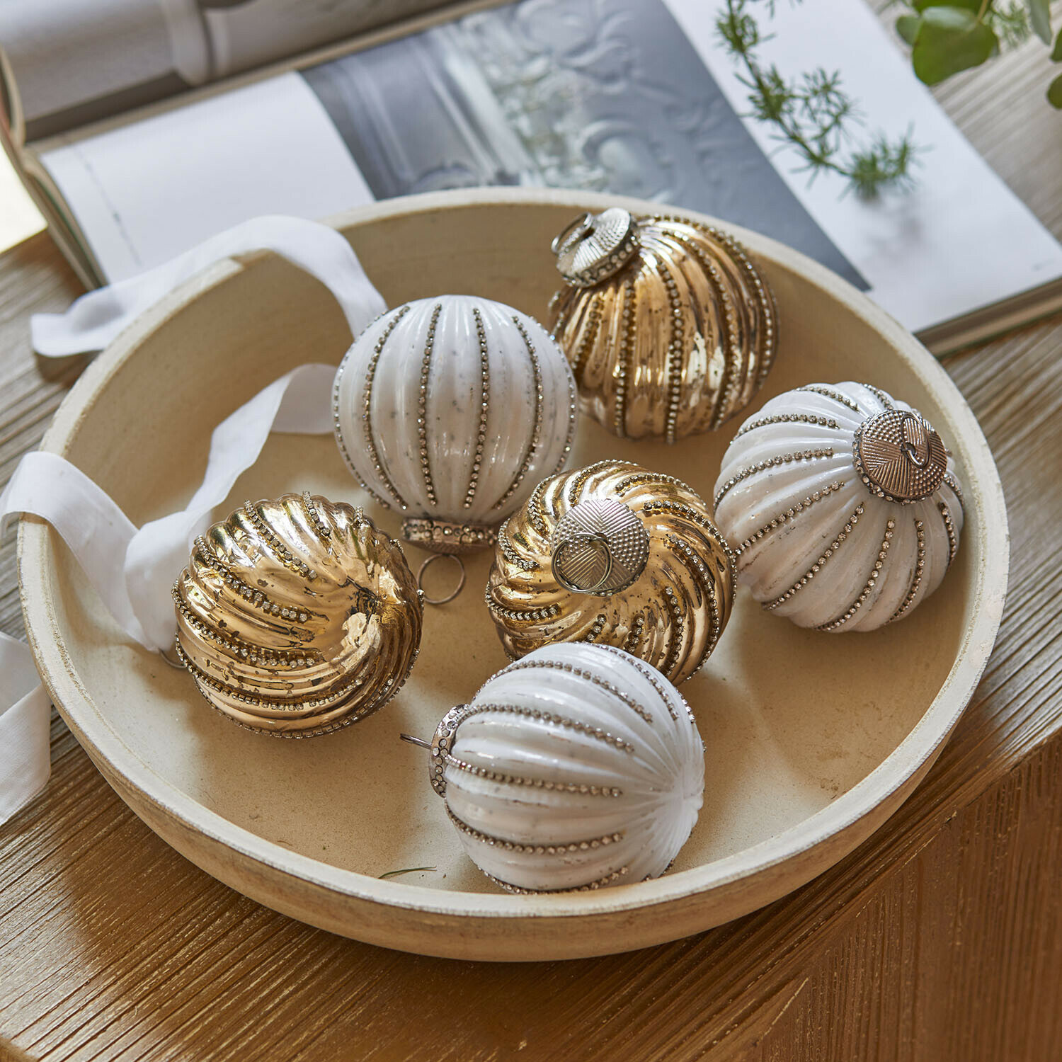 Weihnachtskugel 6er Set Shaela Set aus weissen und goldfarbenen Weihnachtskugeln mit metallischem Glanz in einer runden Schale auf Holztisch