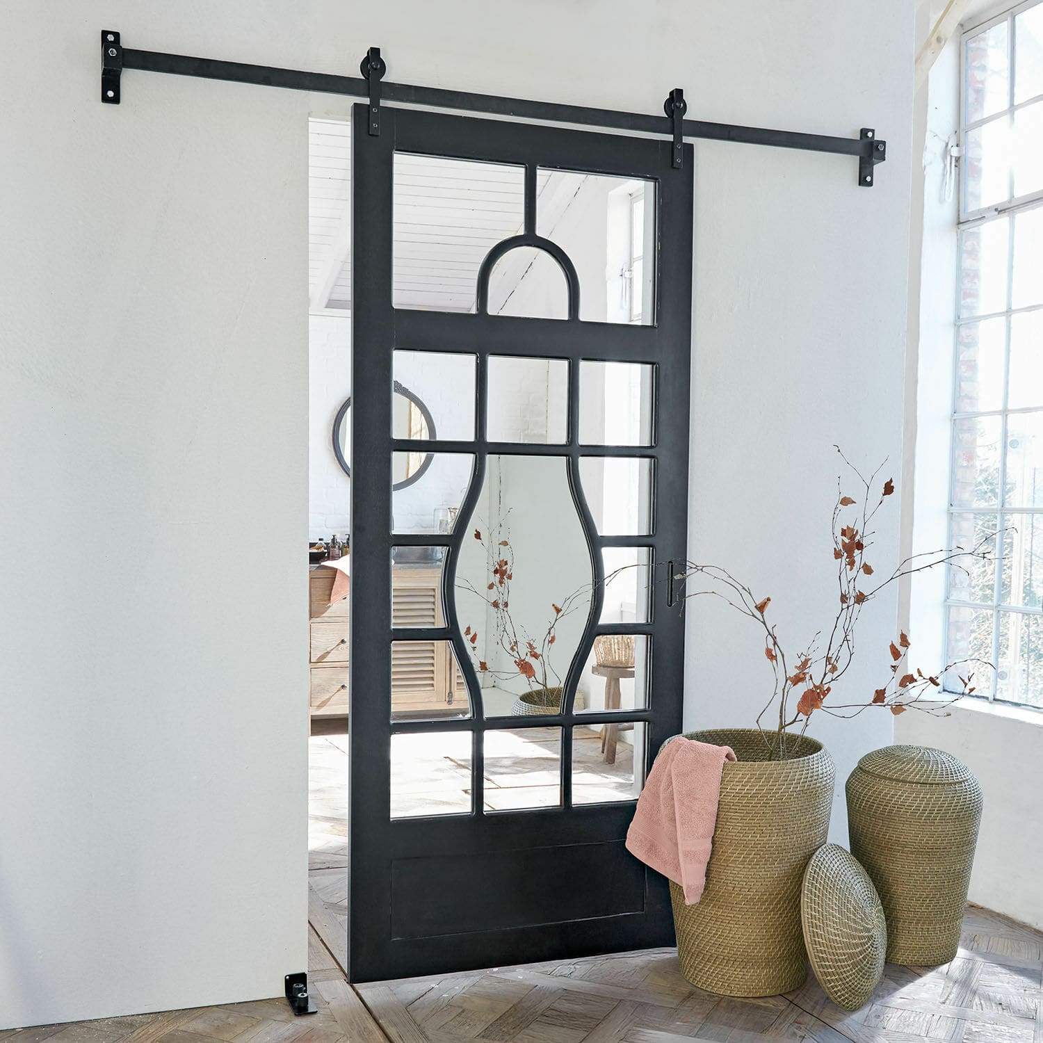 Schiebetür Wilmorton Schwarze Metall-Schiebetür mit geometrischem Spiegelmuster in hellem Raum mit Korb aus Rattan.