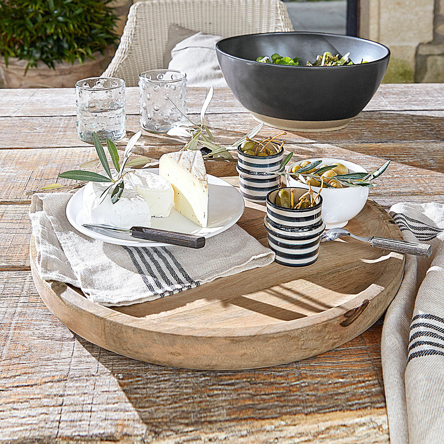 Runde Holzservierplatte mit Käse, Oliven und Keramiktassen auf rustikalem Holztisch