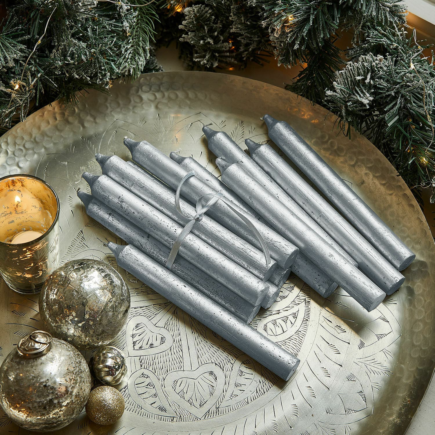 Kerze 20er Set Lysarion Silberne Stabkerzen auf einer Messingplatte mit Weihnachtsdekoration und Kugeln vor grünen Zweigen