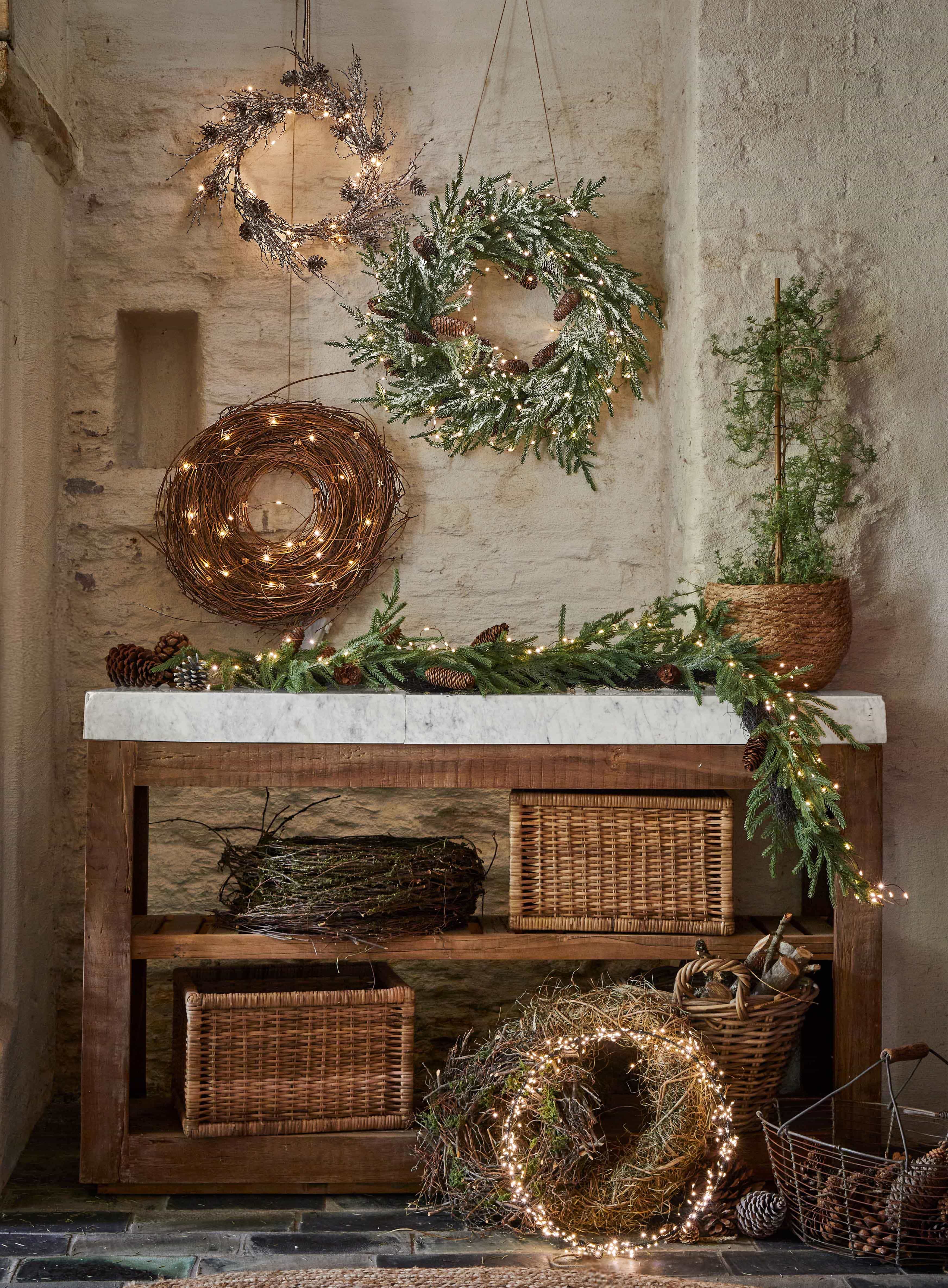 Dekorative Weihnachtskränze aus Zweigen, Zapfen und Lichterketten auf Holztisch in rustikalem Raum