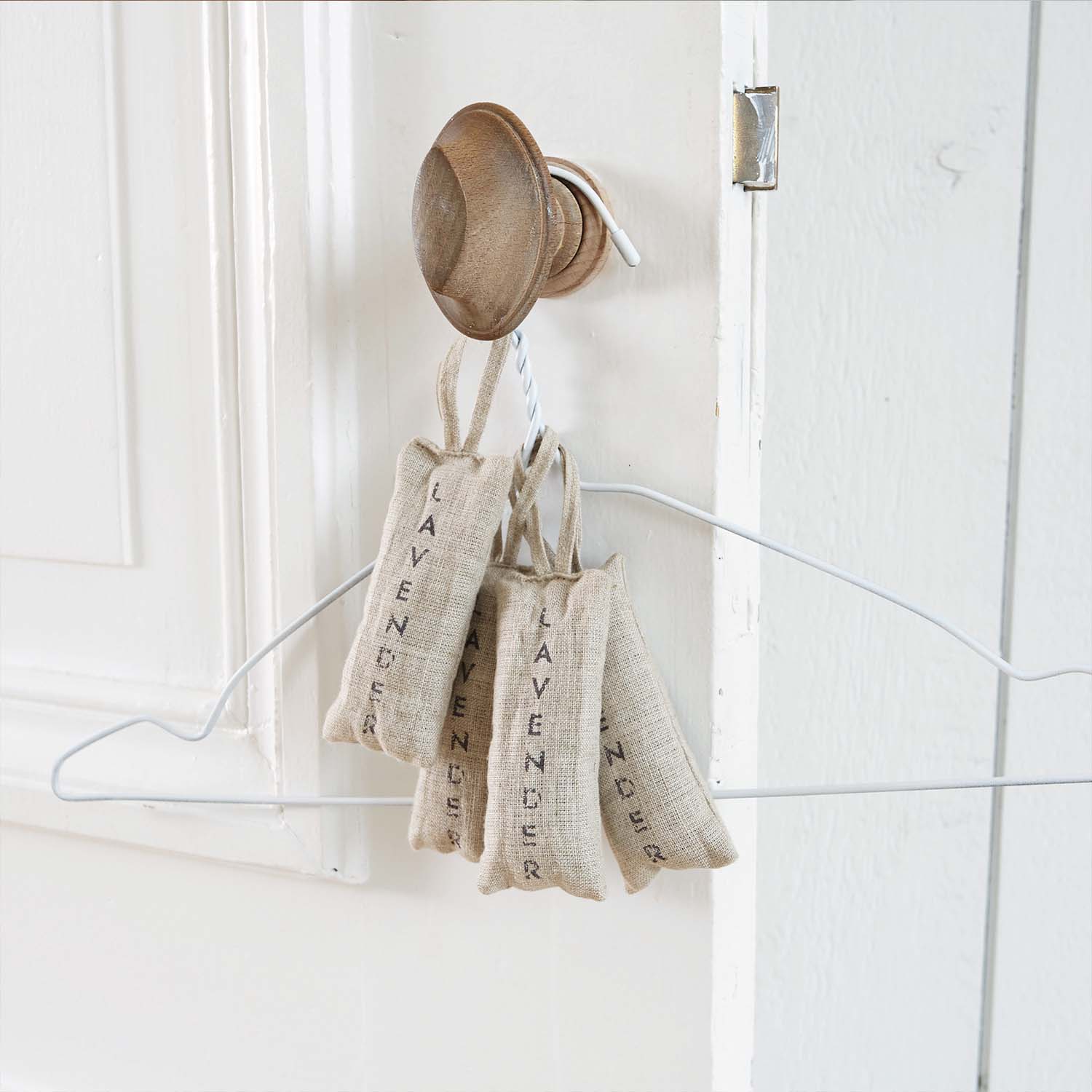 Leinenbeutel mit Lavendel in Naturfarbe an Holzhaken an weisser Tür hängend