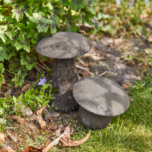Dekorative graue Betonpilze im Garten auf Gras mit grünen Pflanzen im Hintergrund