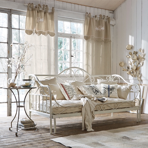 Weisse Metallsofa mit beigen Kissen und hellen Vorhängen in rustikalem Wohnzimmer