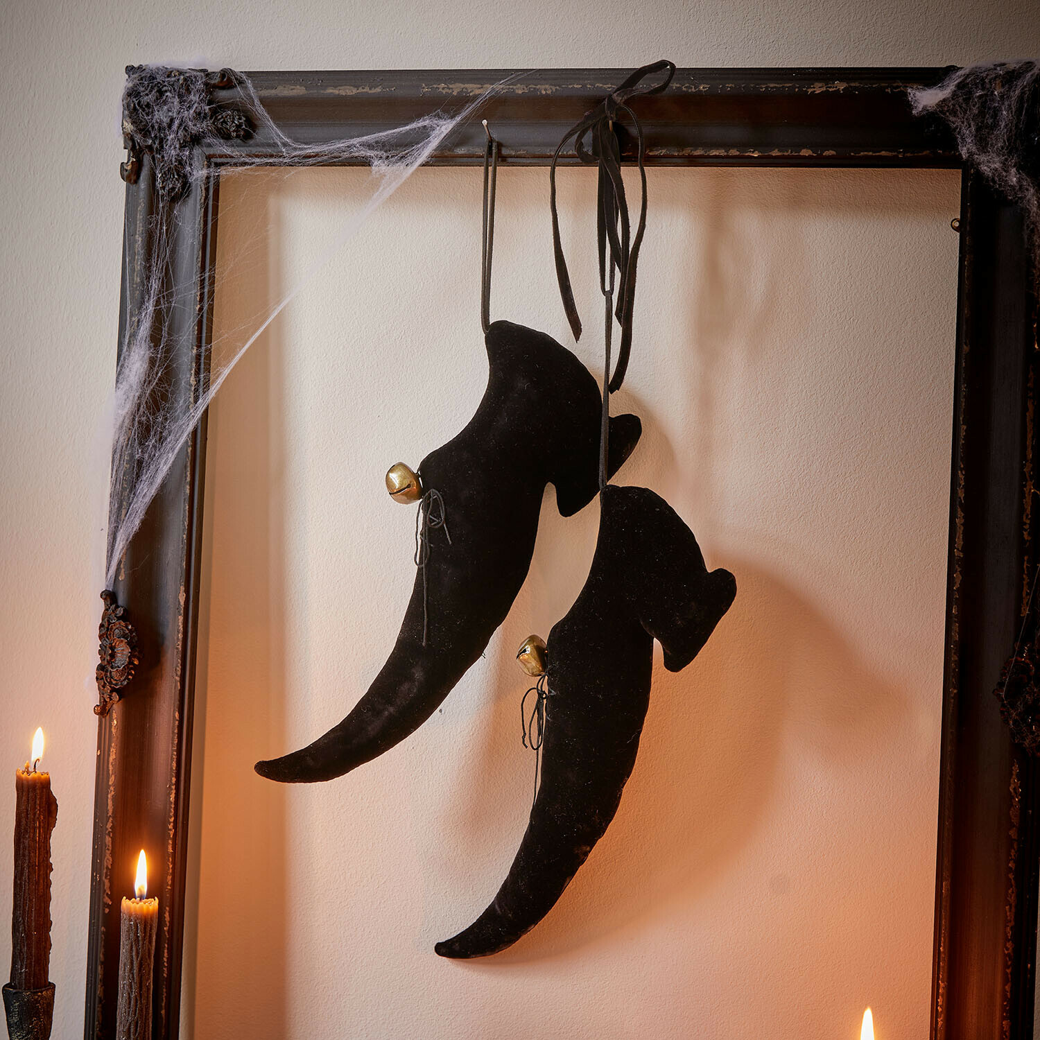 Deko-Schuh 2er Set Trésalya Schwarze Samt-Hexenschuhe mit Glöckchen, hängend an einem antiken Rahmen mit Spinnweben und Kerzen