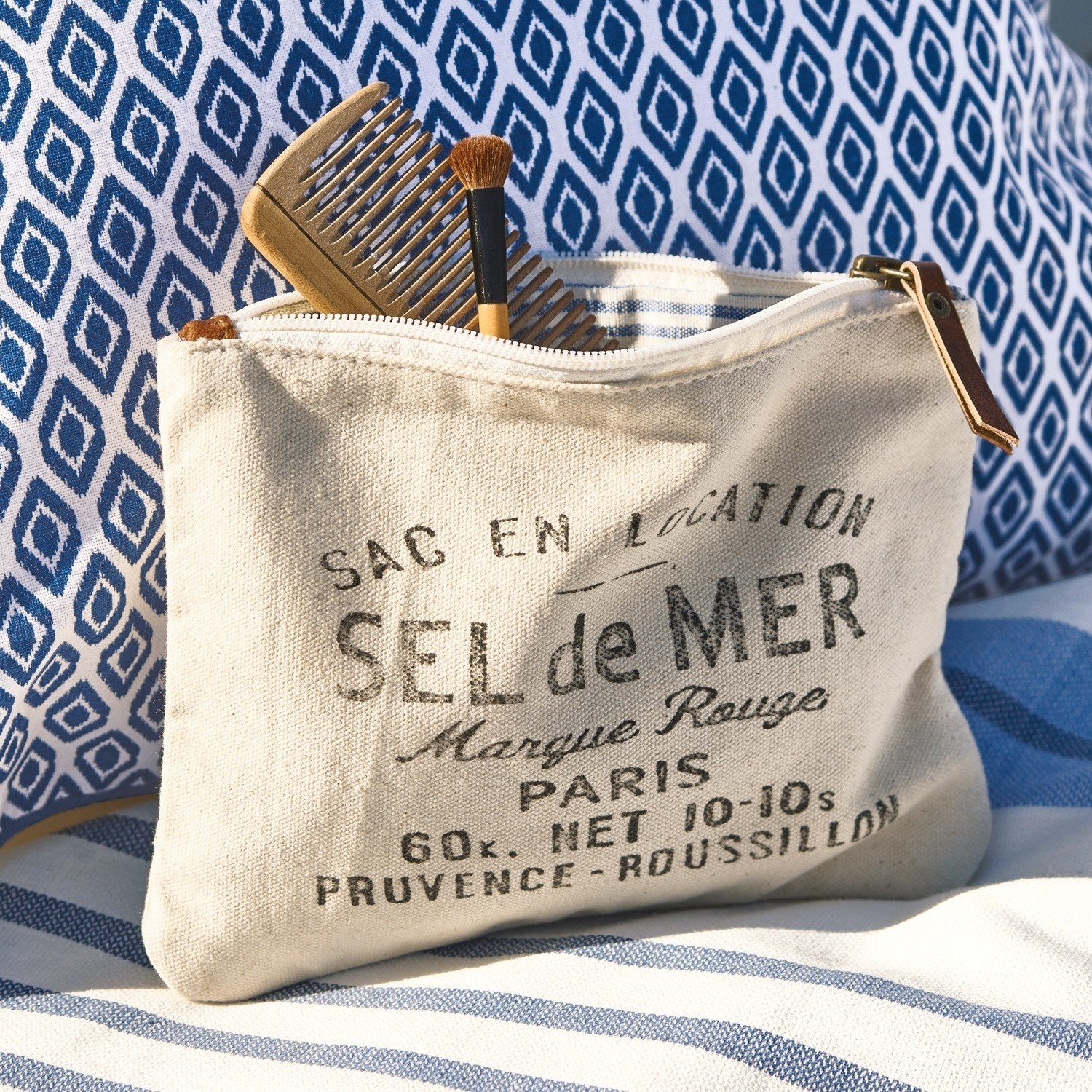 Täschchen Sel de Mer Beige Kosmetiktasche aus Baumwolle mit Aufdruck und Leder-Reissverschluss vor blau-weiss gestreiftem Stoff
